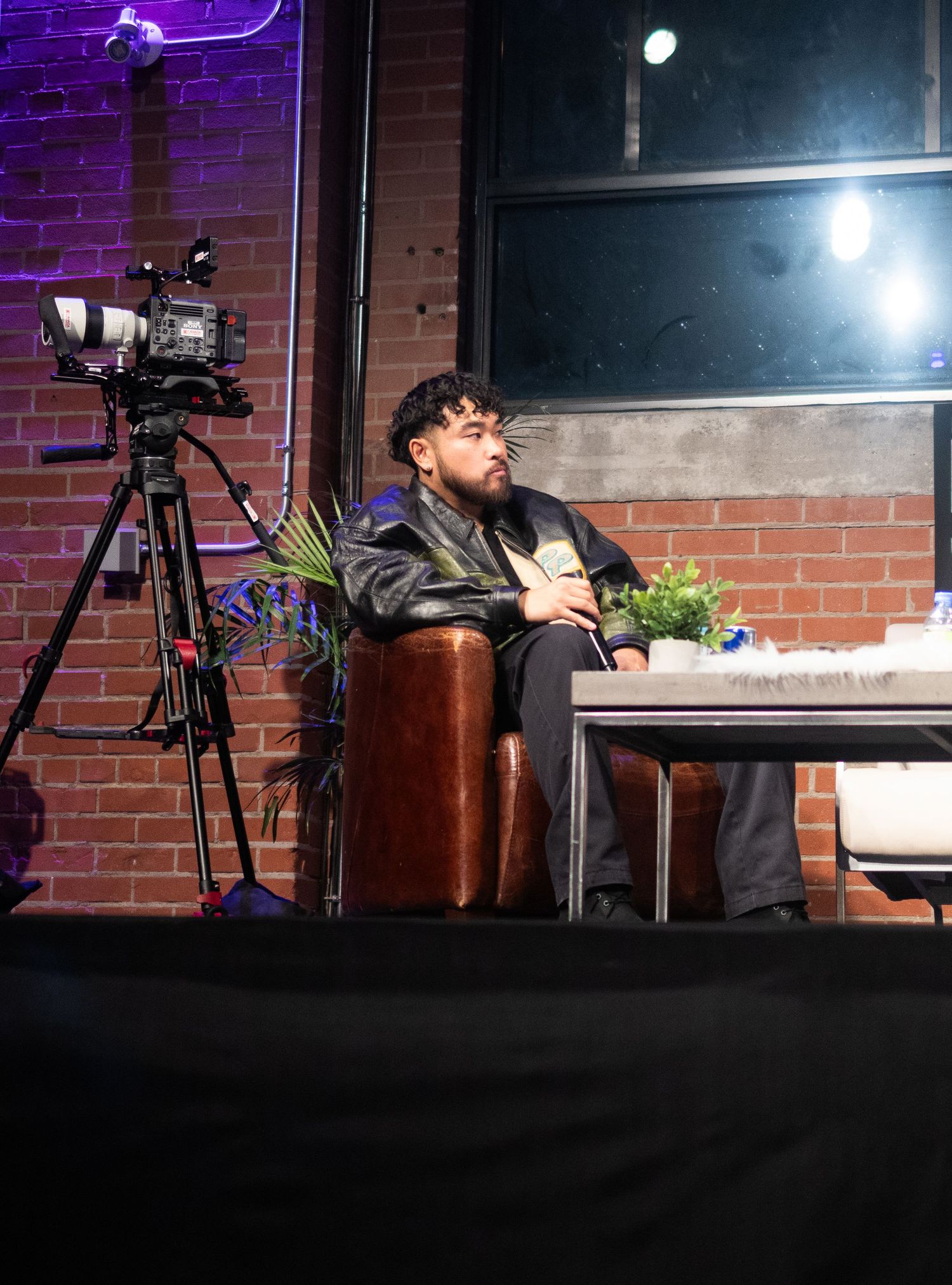 Camera setup and person seated at table in brick-walled venue with mood lighting.