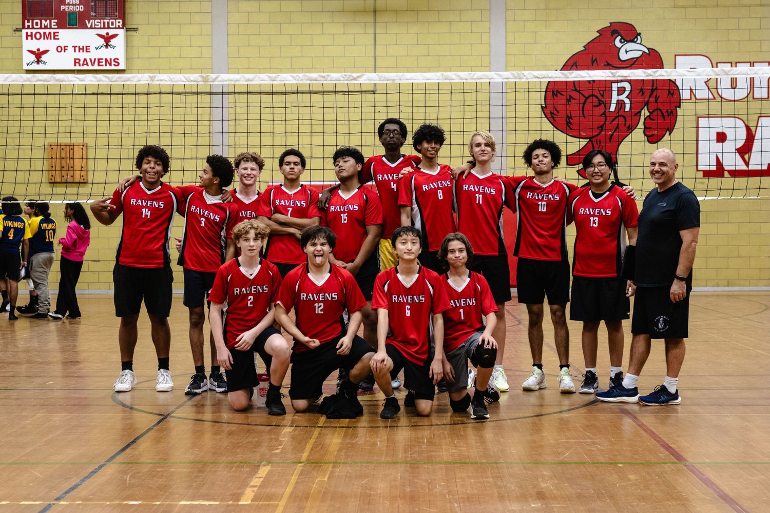 A volleyball team in red uniforms poses together for a group photo in a gymnasium.
