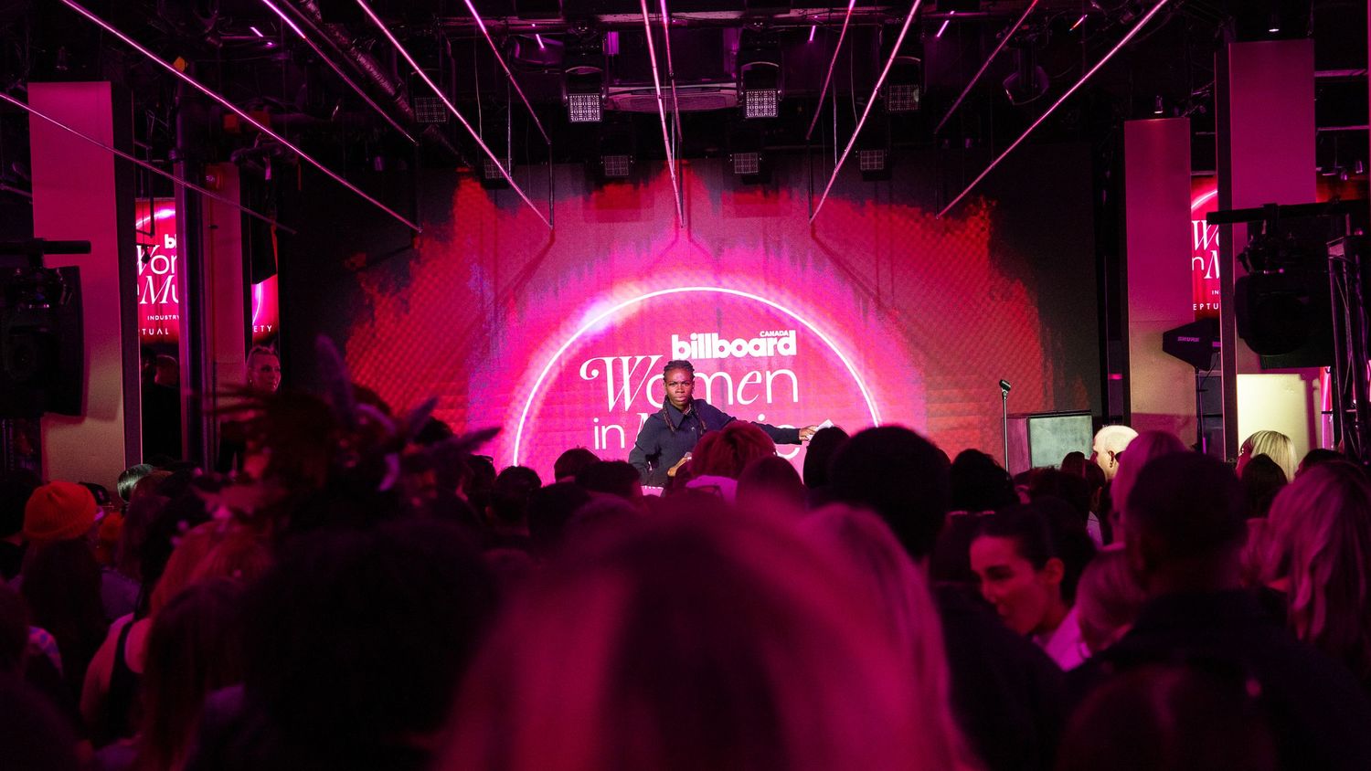 A crowded nightclub with pink neon lighting and a glowing arch on the stage.
