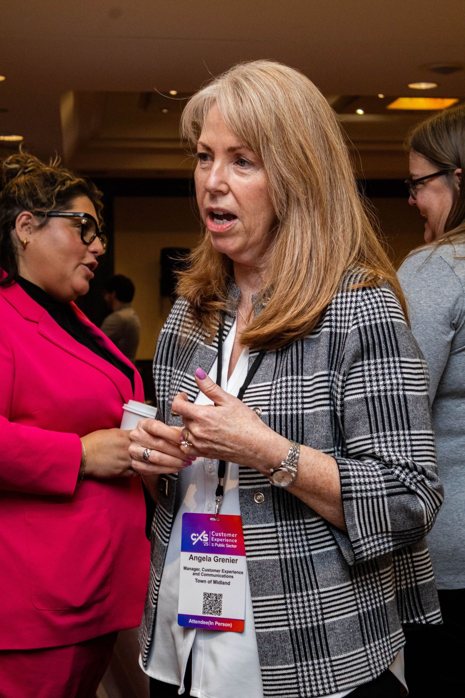 Two attendees engage in conversation at a professional conference, with one wearing a pink blazer and another in plaid.