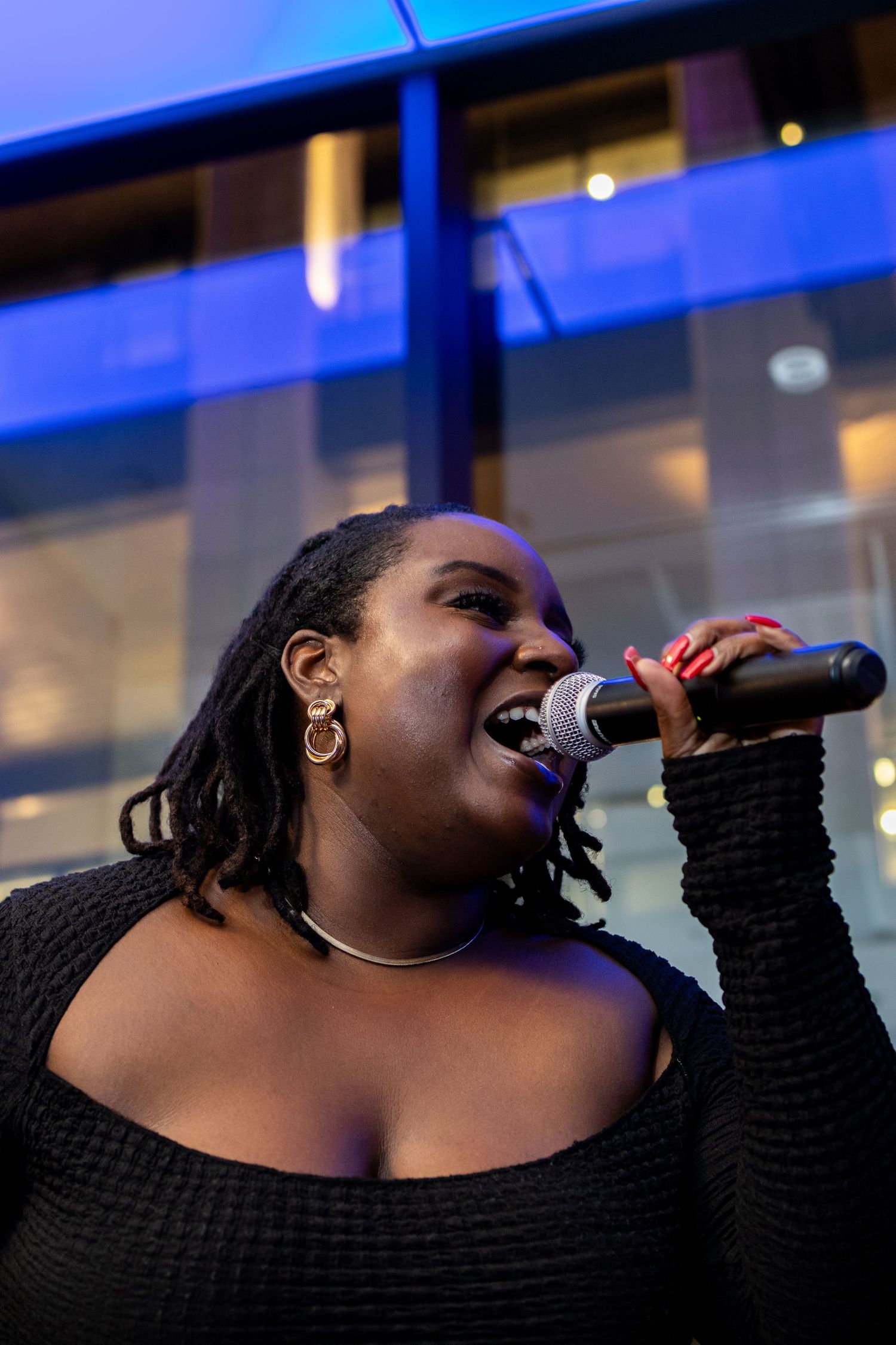 A performer in black sings passionately into a microphone against a blue-lit backdrop.