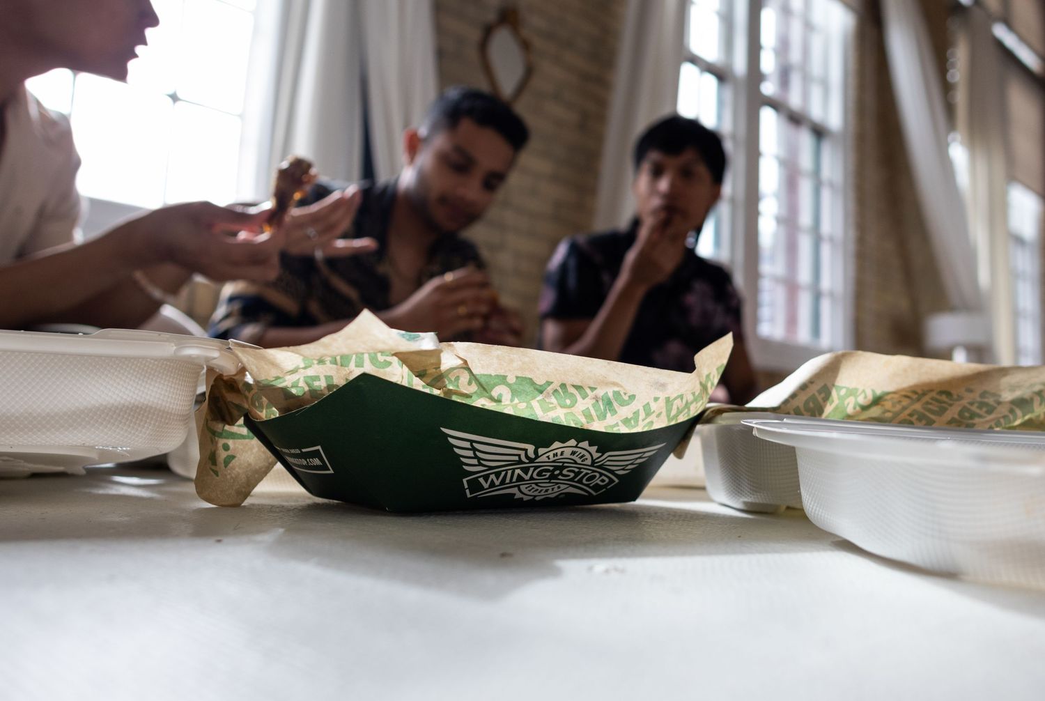 People share meal with wrapped sandwiches on table during casual gathering.