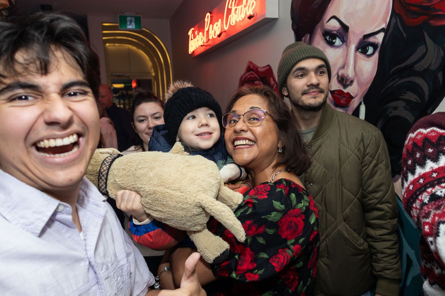 Lively group photo with stuffed bear at entertainment venue with wall mural.