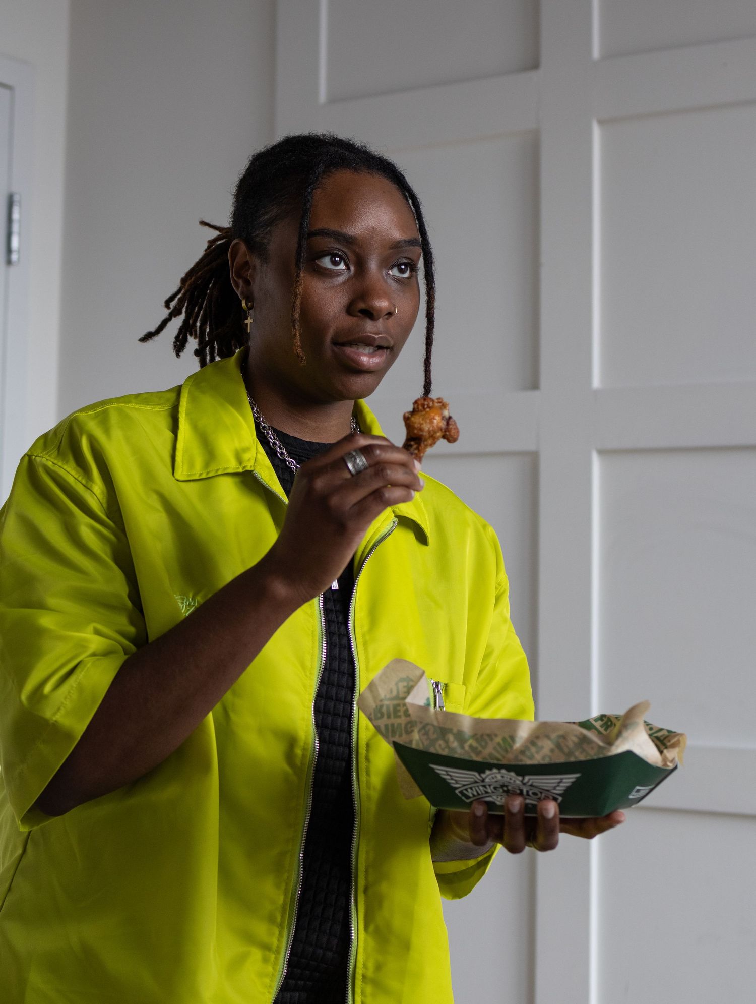 Person in bright yellow jacket eating from a food container indoors.