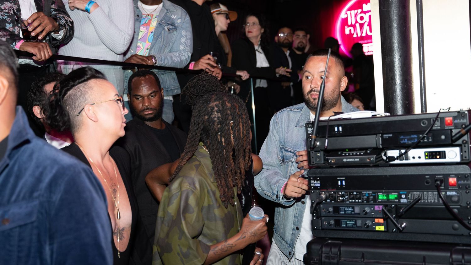 Performers and guests gathering around DJ equipment at a nightclub event.