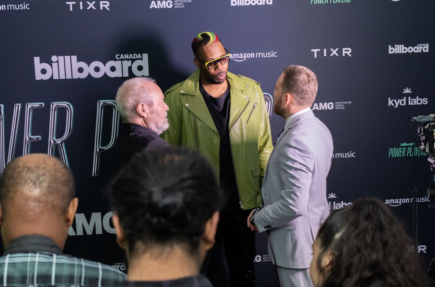 Celebrity on red carpet wearing olive green jacket at Billboard event.