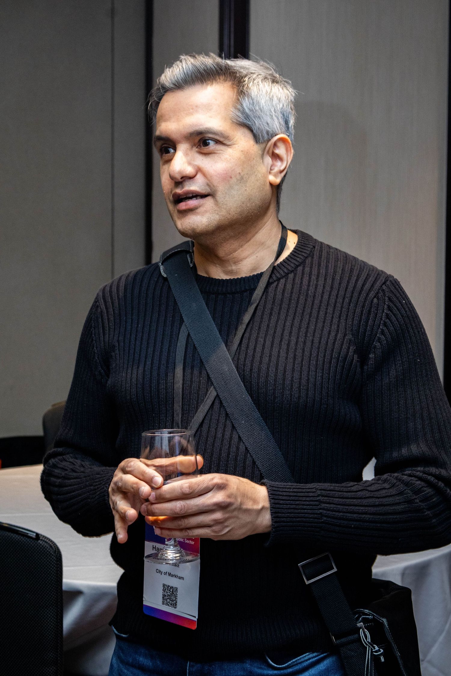 Conference attendee in black sweater holds beverage while networking at event.