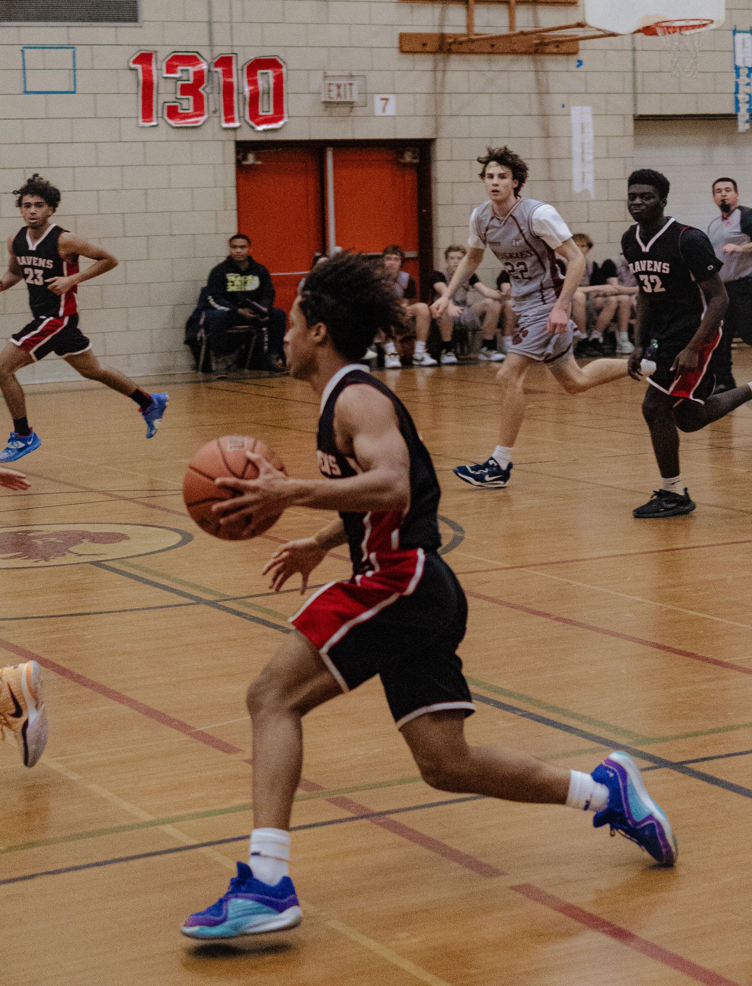 Basketball players compete intensely during an indoor game on a wooden court with red jerseys.