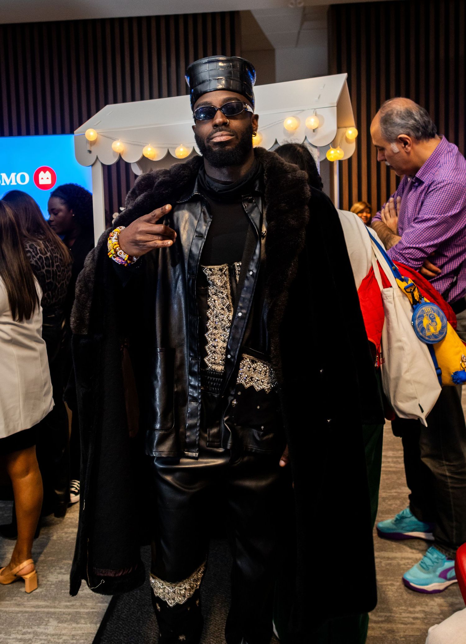 A performer wearing black and gold attire with sunglasses poses at an indoor event.