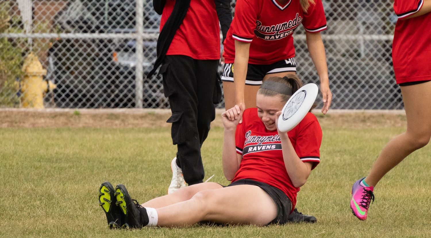Injured athlete sitting on grass field surrounded by teammates in red uniforms.