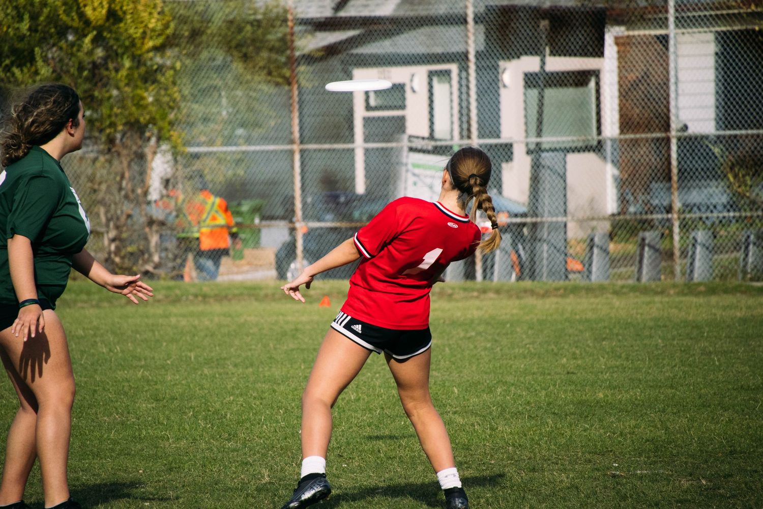 Two players practicing on a grassy field with one in a red uniform.