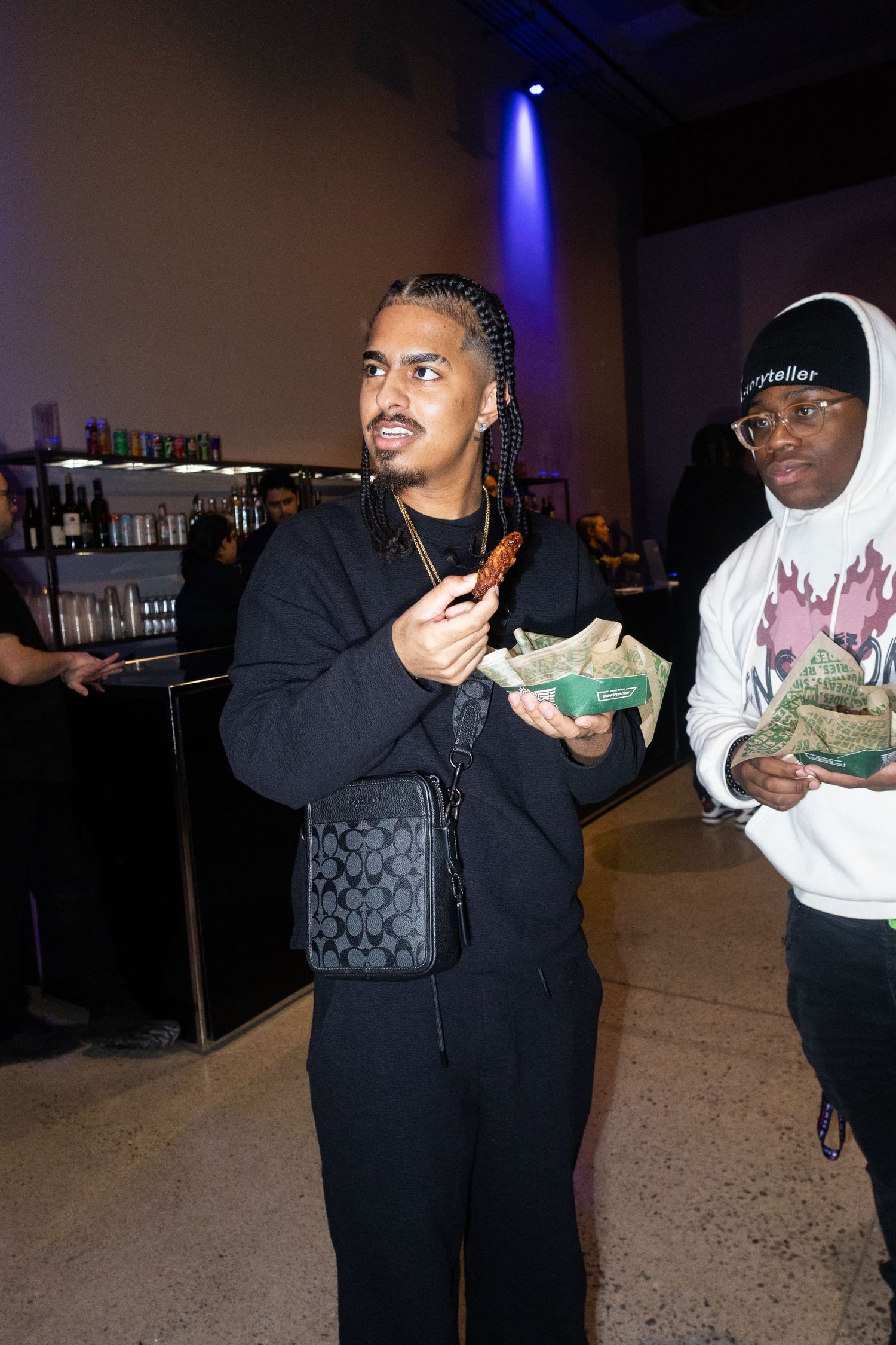 People holding food items at a dimly lit indoor venue.