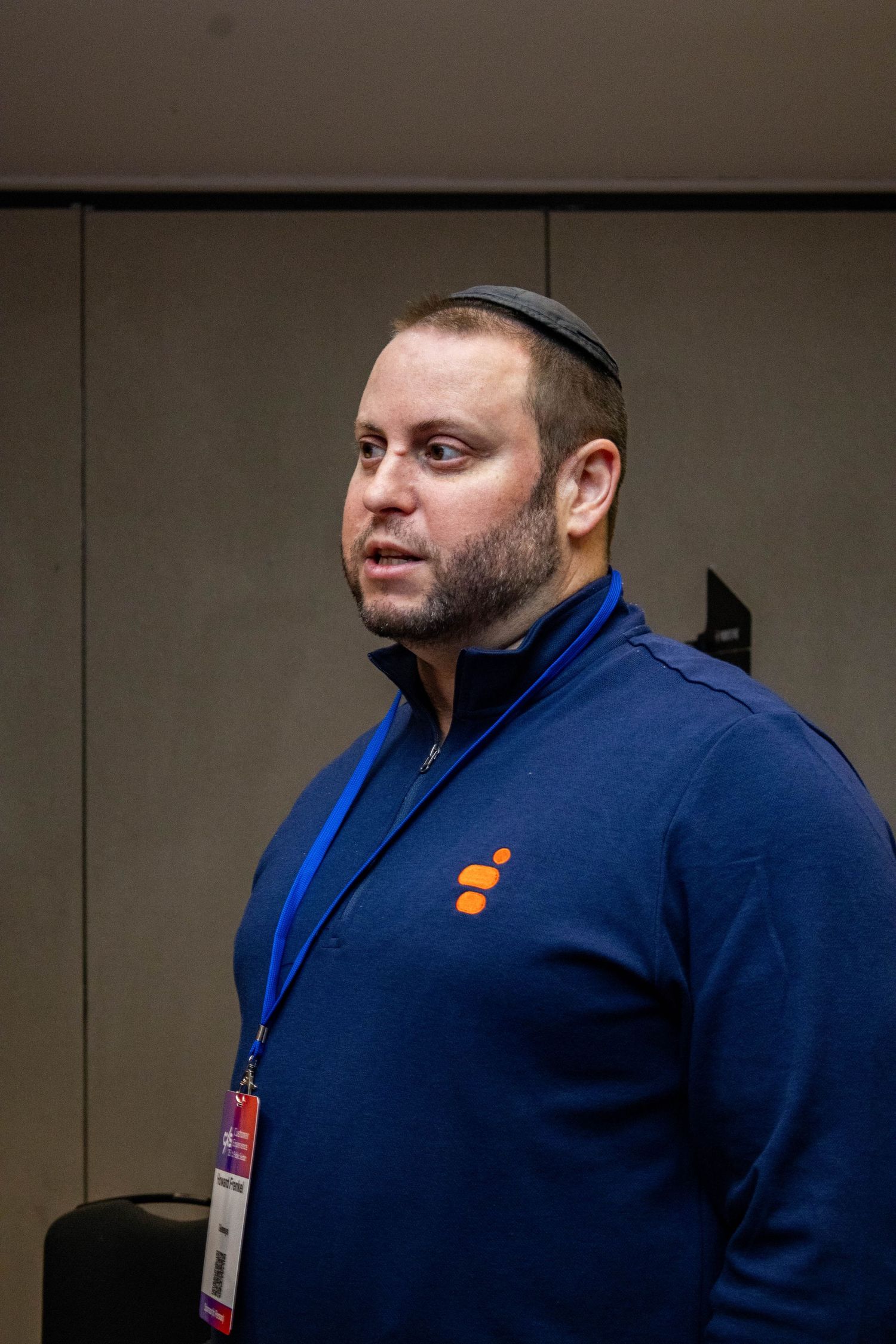 Security personnel wearing yarmulke and navy jacket stands in professional setting.