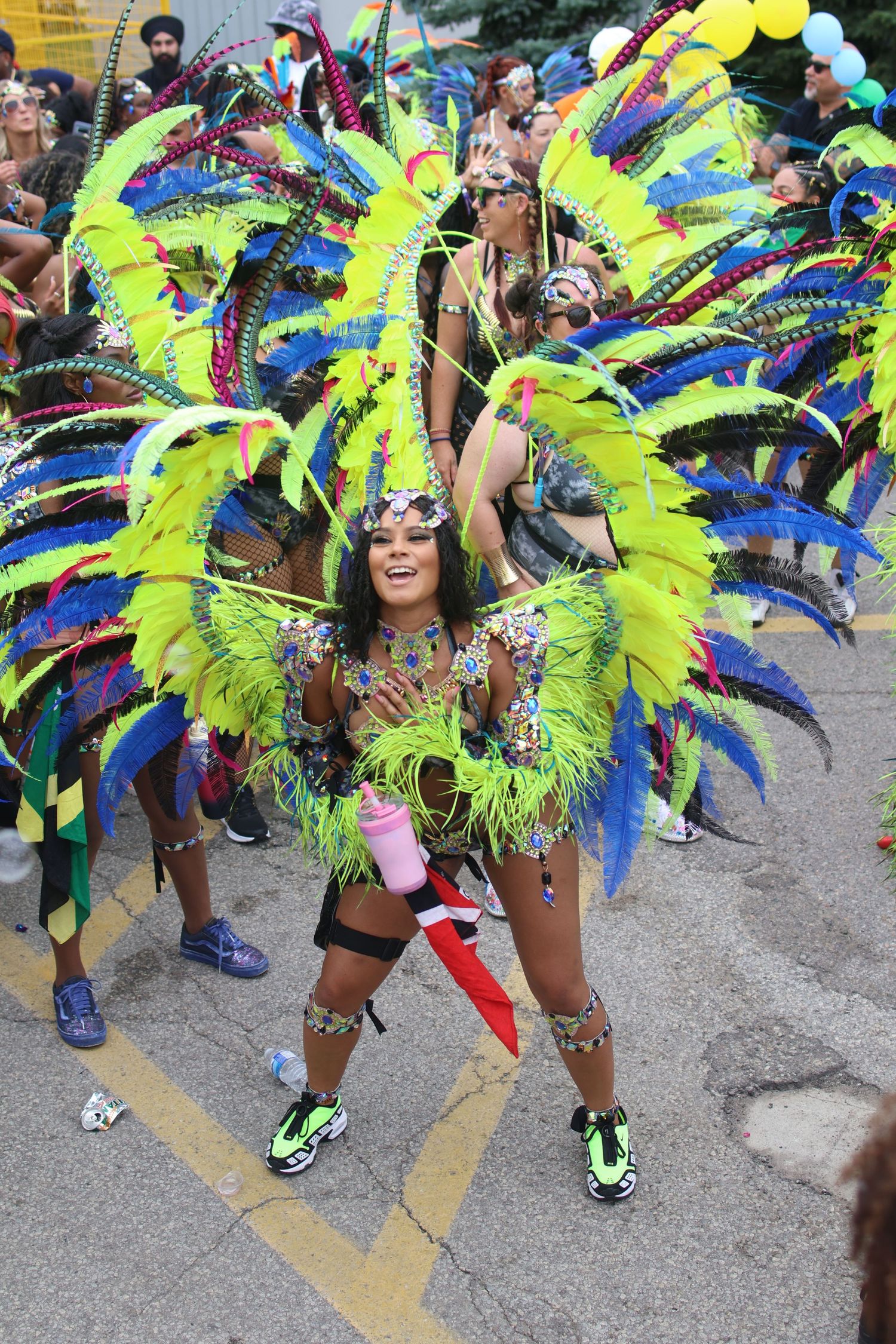 Carnival dancer wearing vibrant green and blue feathered costume performs at outdoor festival.