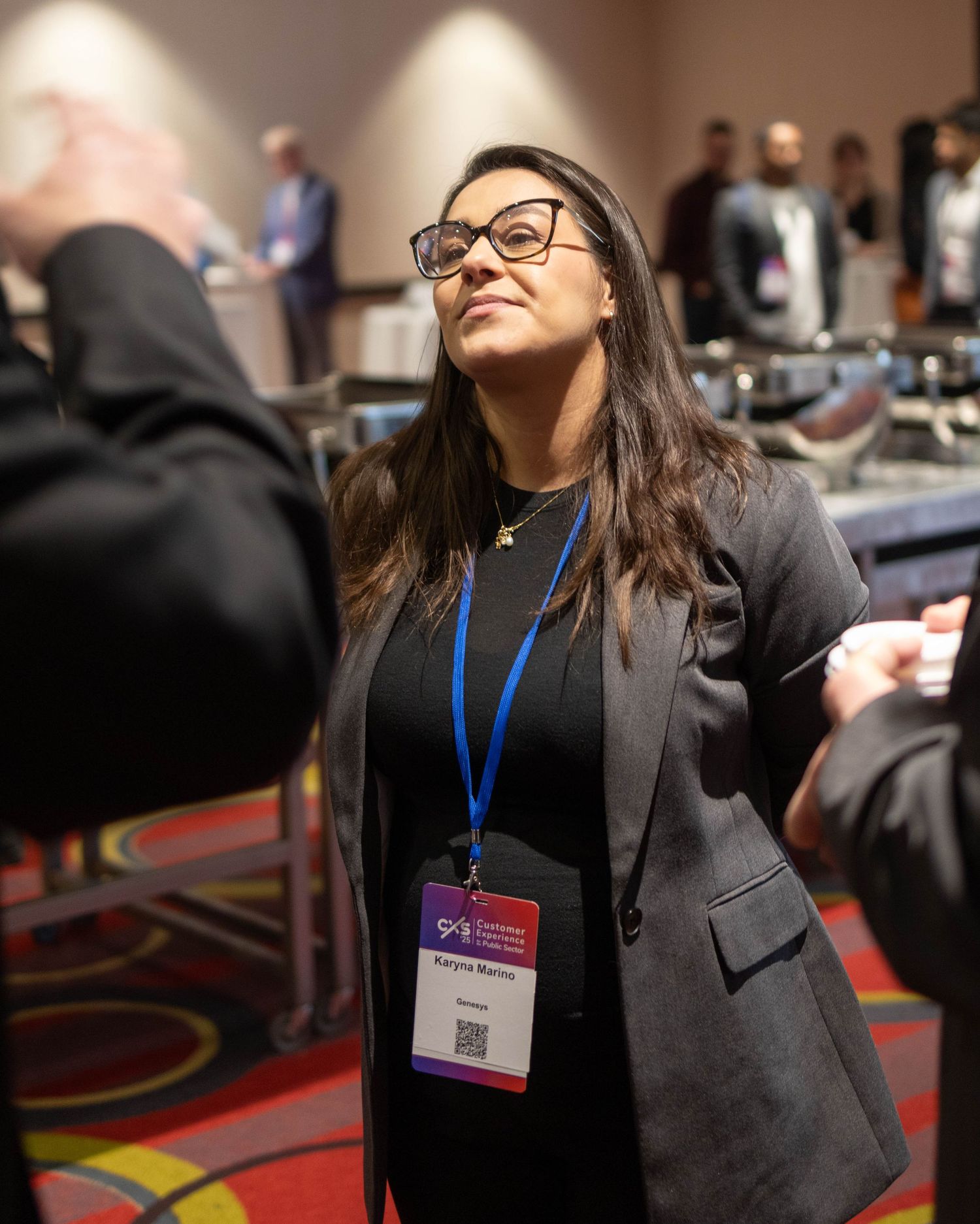 Professional attendee wearing black blazer and glasses stands in conference room with patterned carpet.