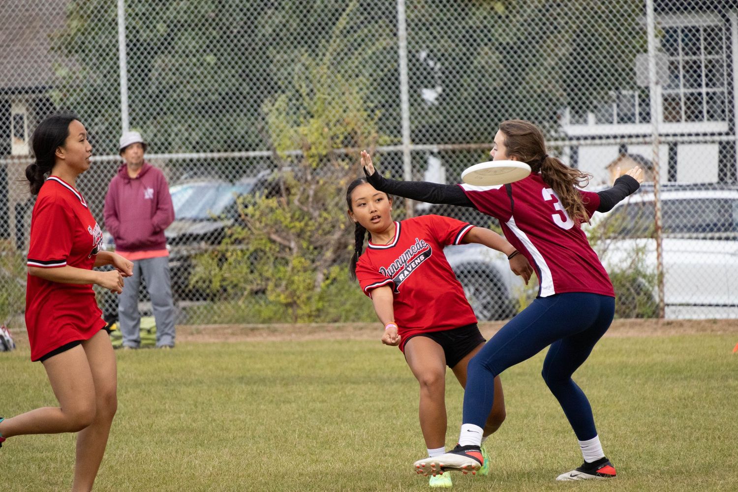 Players in red uniforms competing during an outdoor sports match on a grass field.