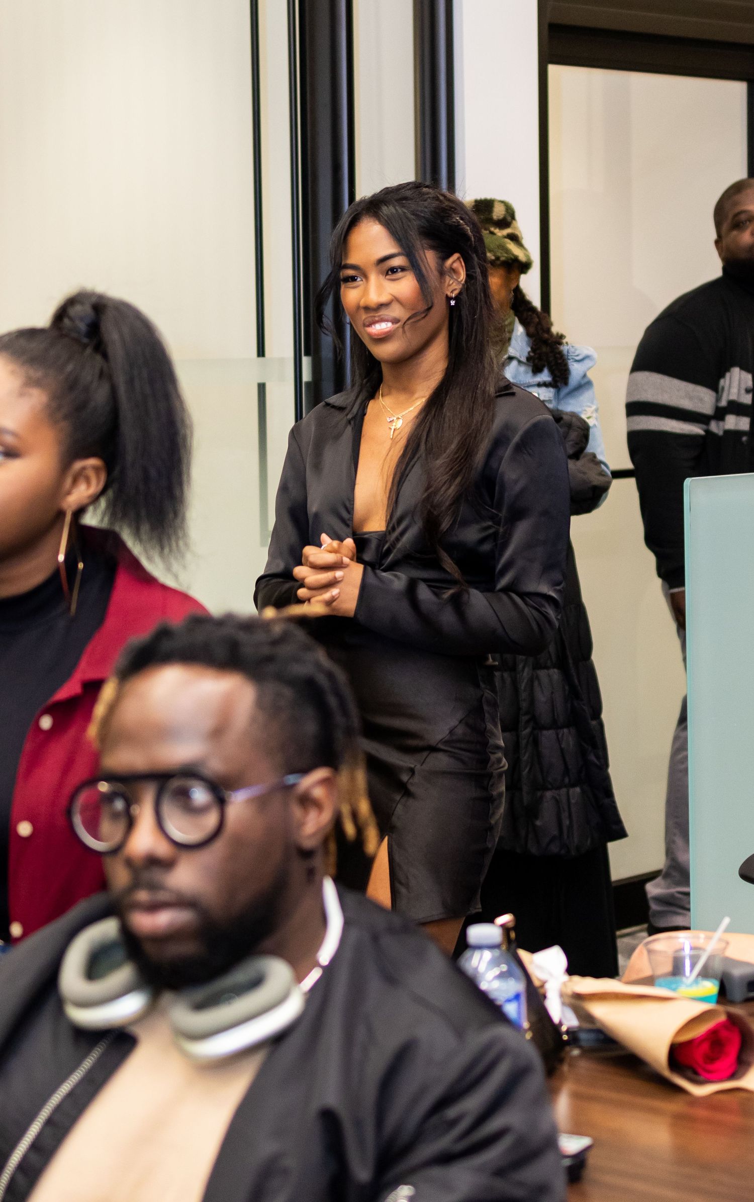 A performer in a black ensemble interacts with the audience during an indoor event.