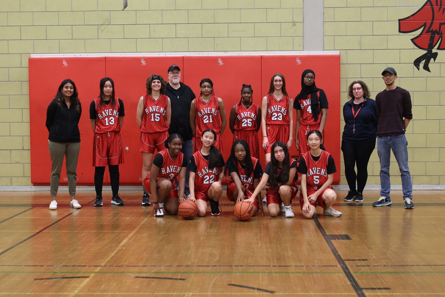 A youth basketball team and coaches pose for a group photo in red uniforms on a gymnasium court.