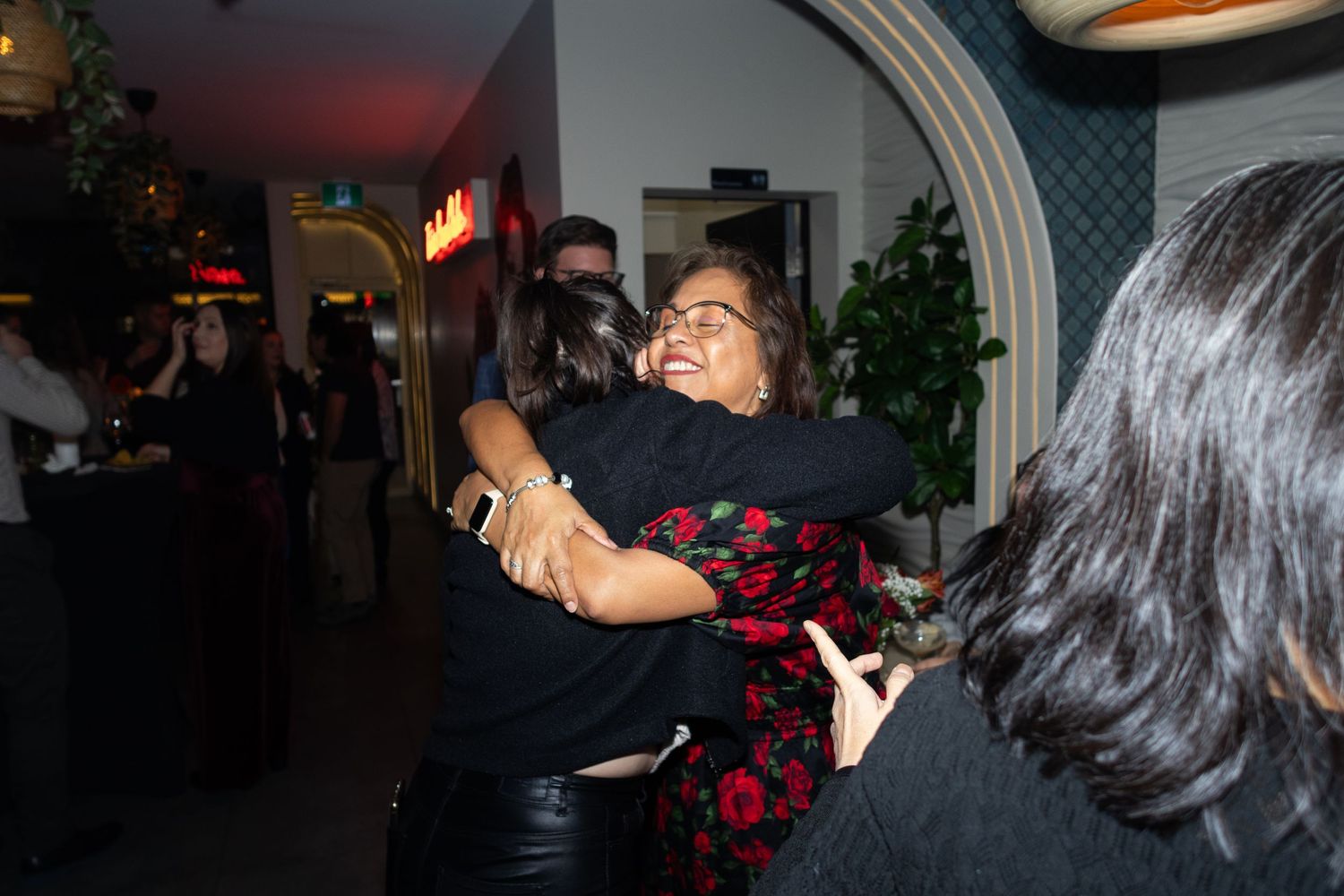 People embracing and celebrating at dimly lit indoor venue with arched doorway.