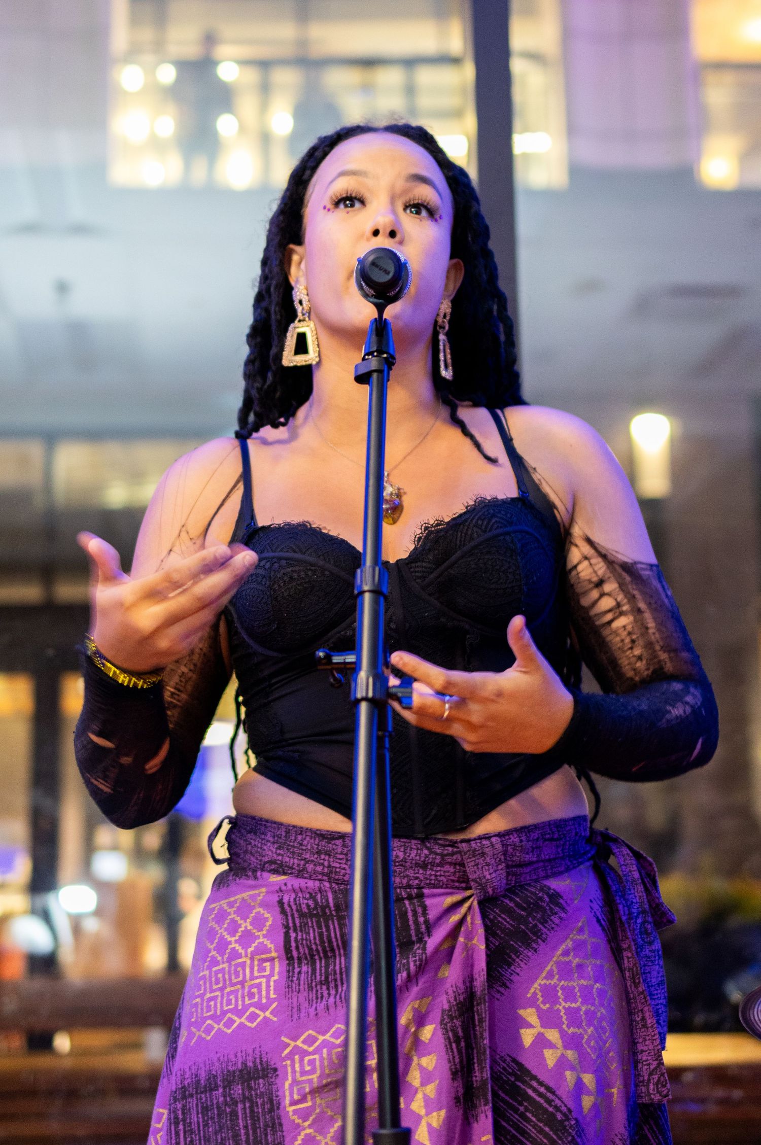 Singer performs passionately in black top and purple patterned pants at nighttime venue.