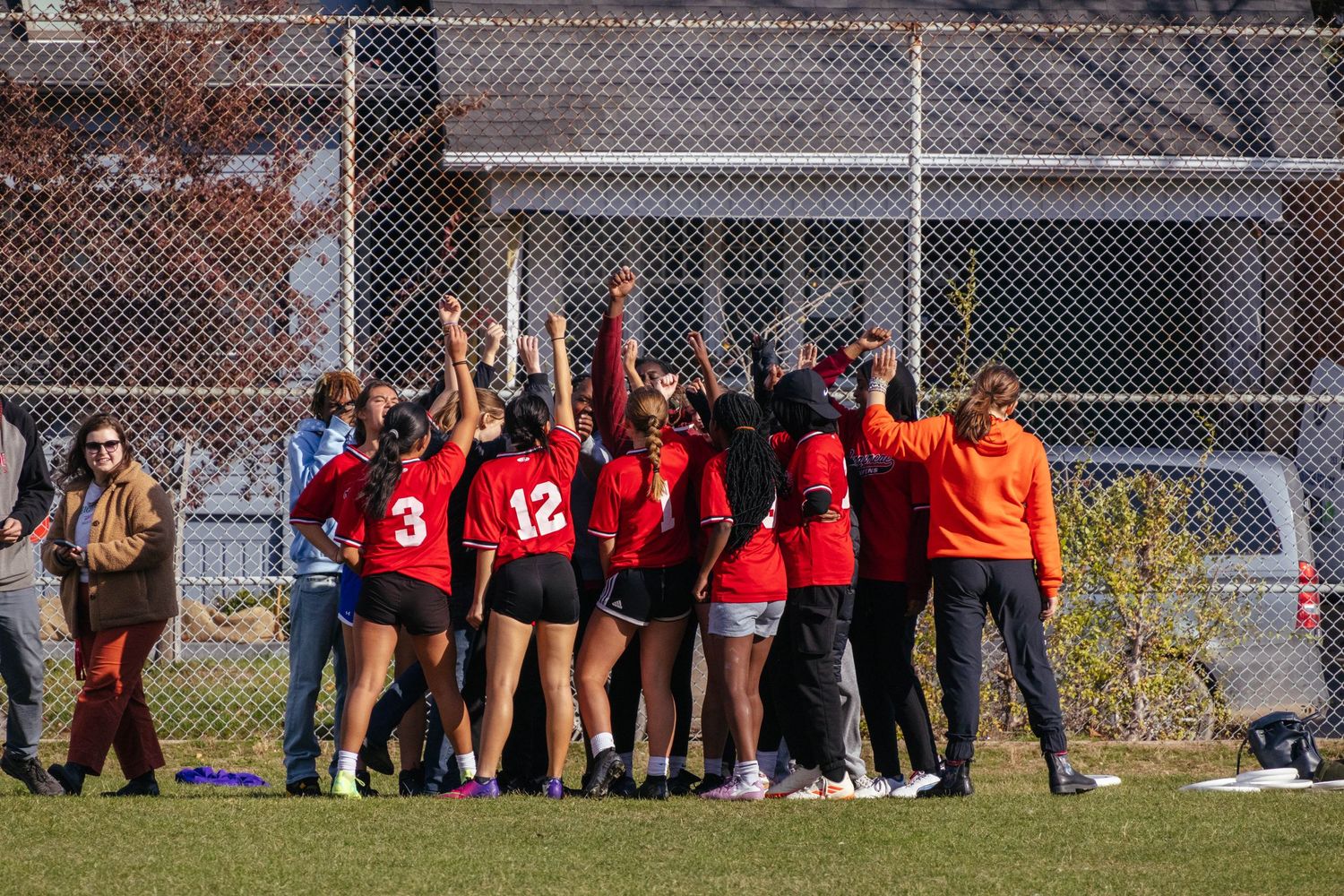 Athletic team in red uniforms huddling together on a grass field during an outdoor sports event.