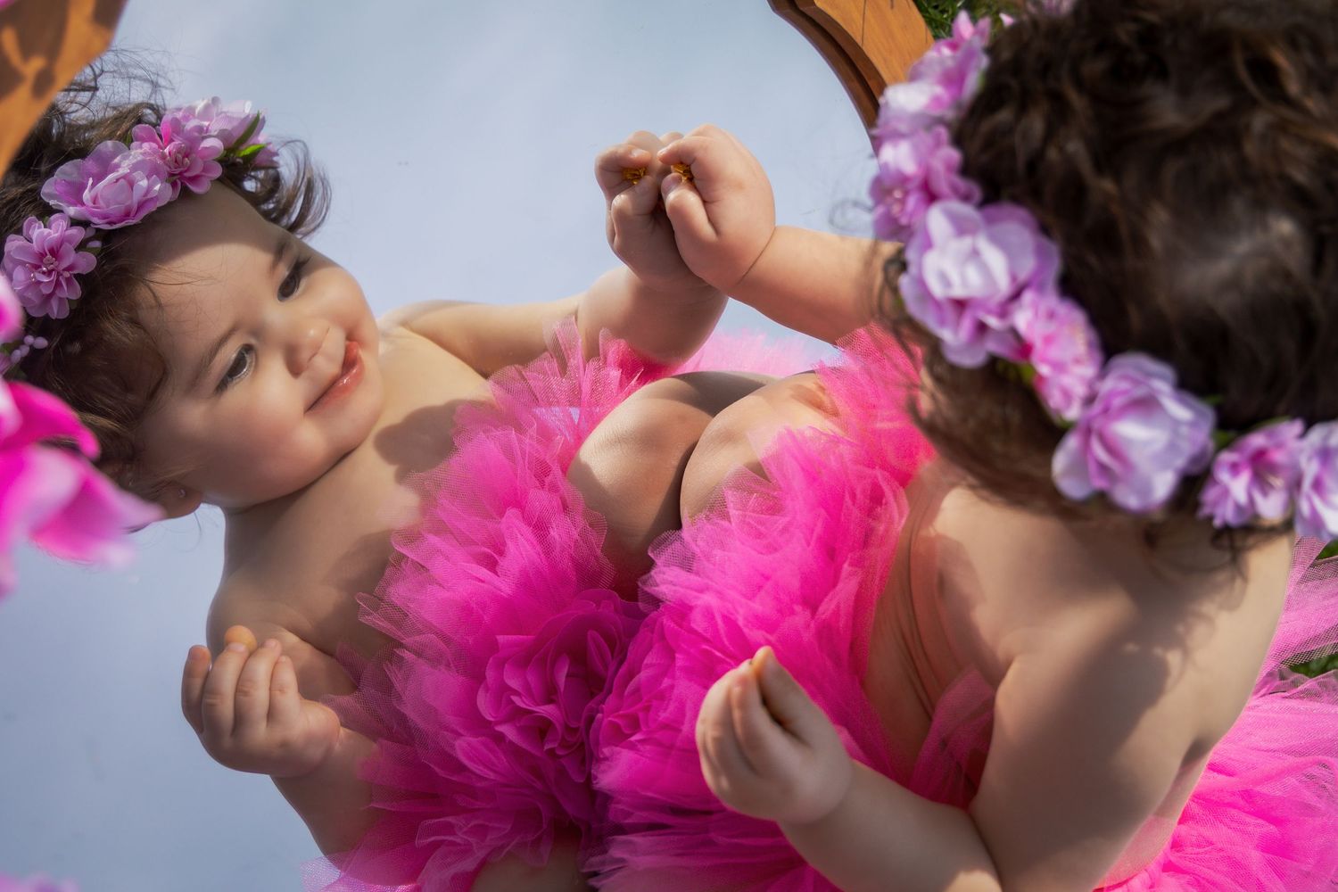 A mirrored reflection showing a pink tutu and purple flower crown against a blue background.