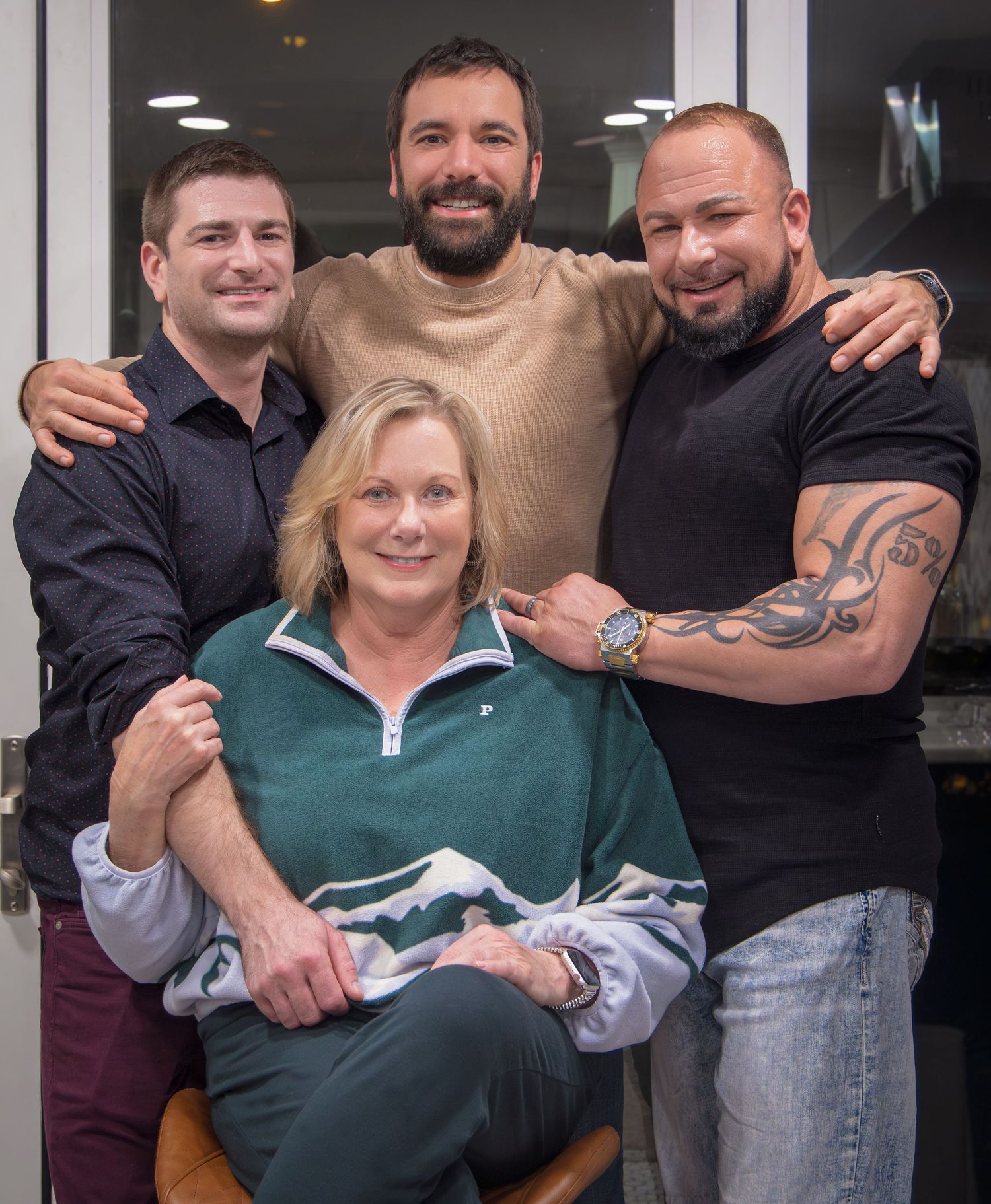 Four people posing together for casual indoor photo with person in beige sweater in center.