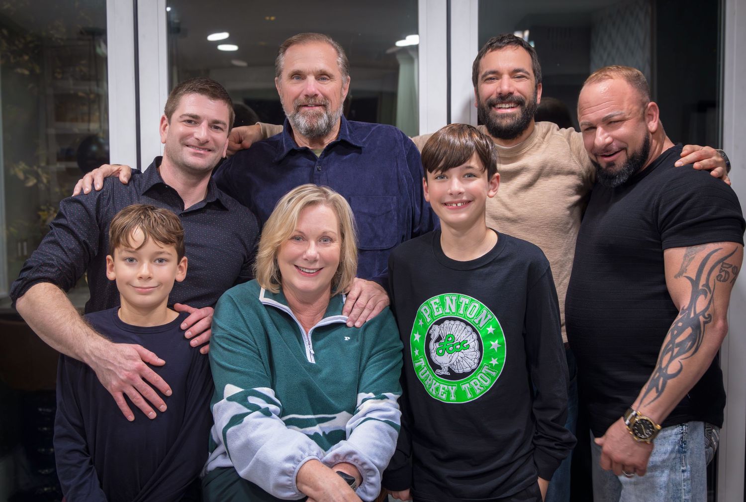 A group of people standing together outdoors in front of glass doors wearing casual clothing.