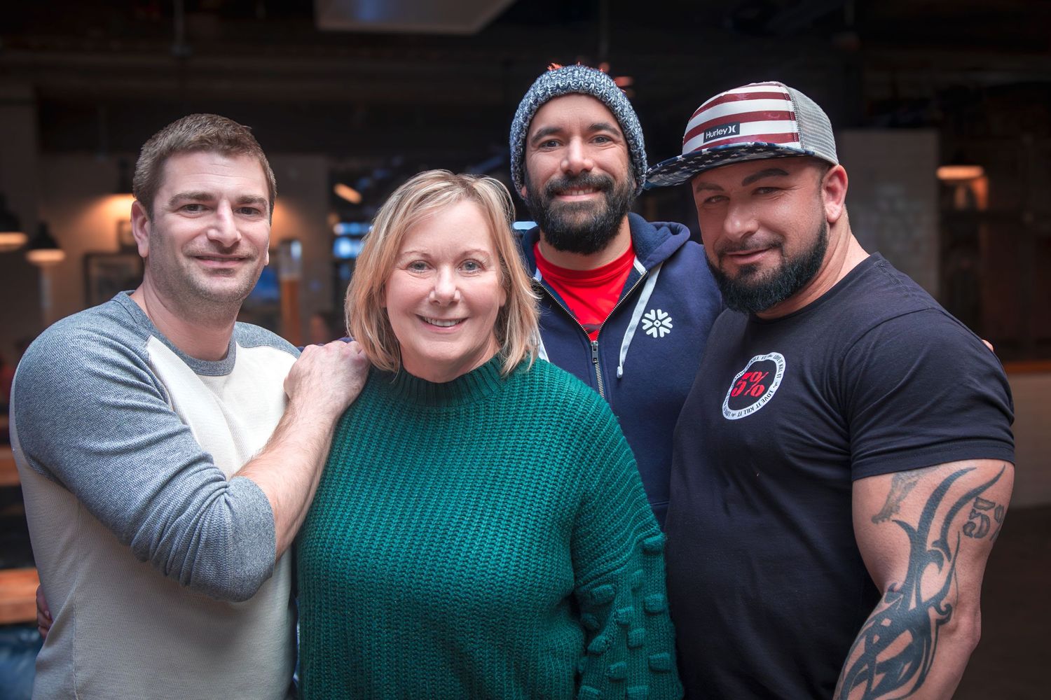 Group photo of four friends posing together in casual attire against dark interior background.