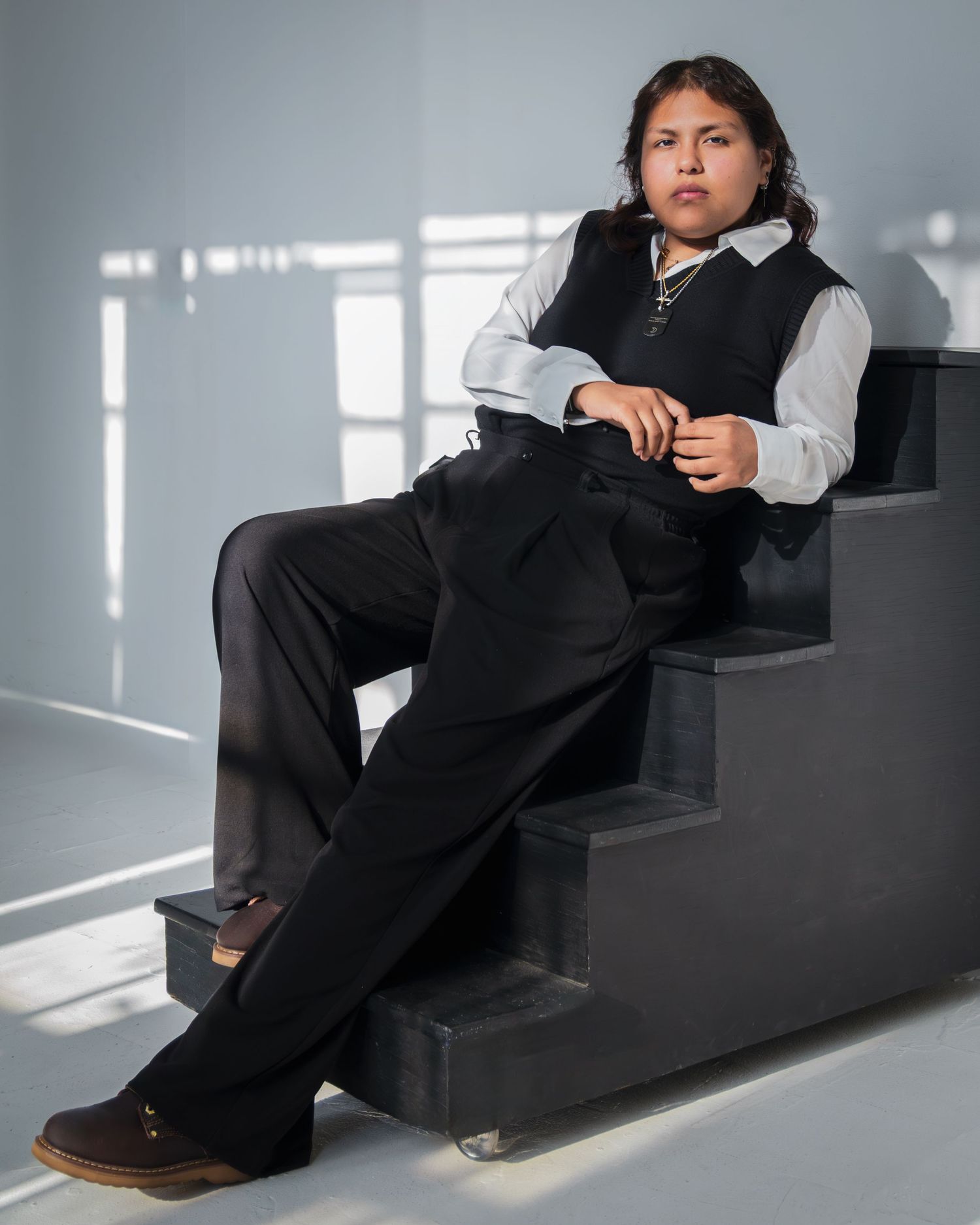 A person in business attire sits on dark stairs in a bright room with dramatic lighting and shadows.