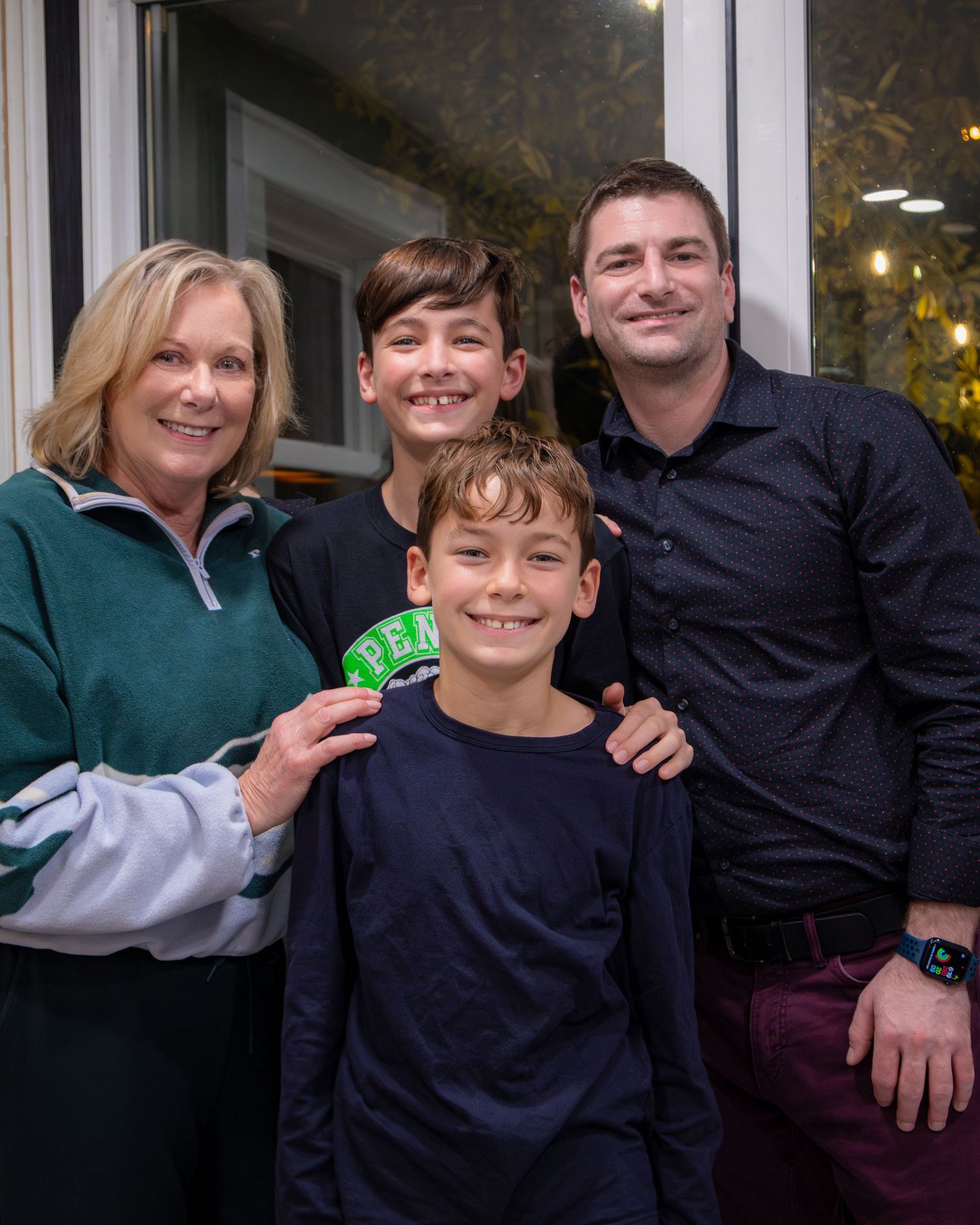 Family of four posing together by a window in casual winter clothing.