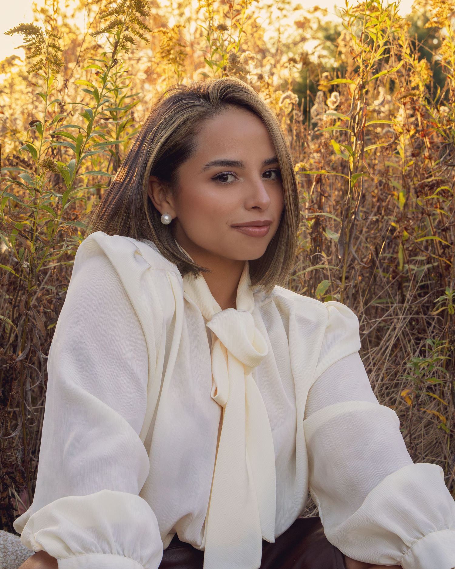 Elegant portrait in a white blouse with bow against golden autumn foliage at sunset.