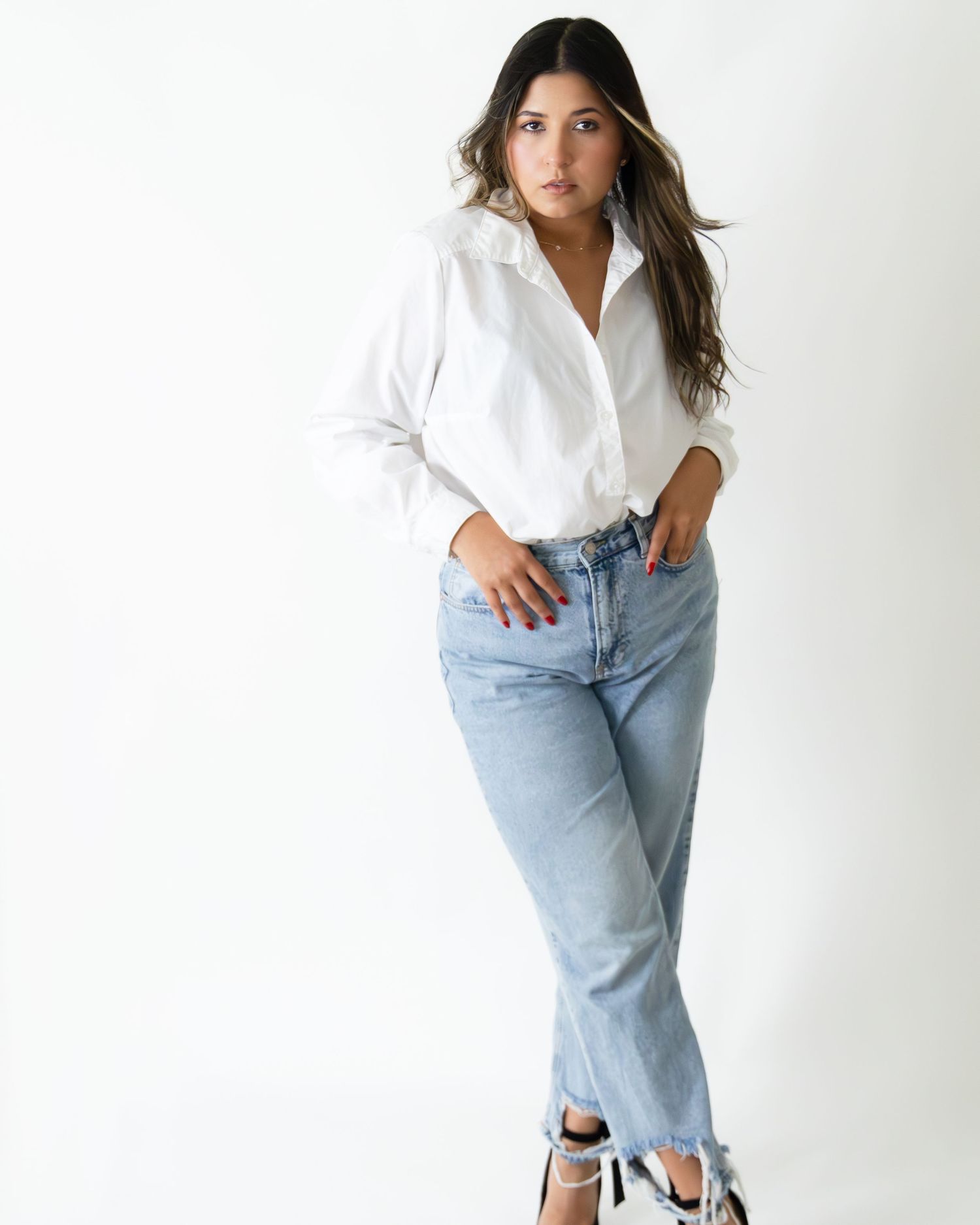 Woman in white button-up shirt and light wash straight-leg jeans with sneakers posing against white background.