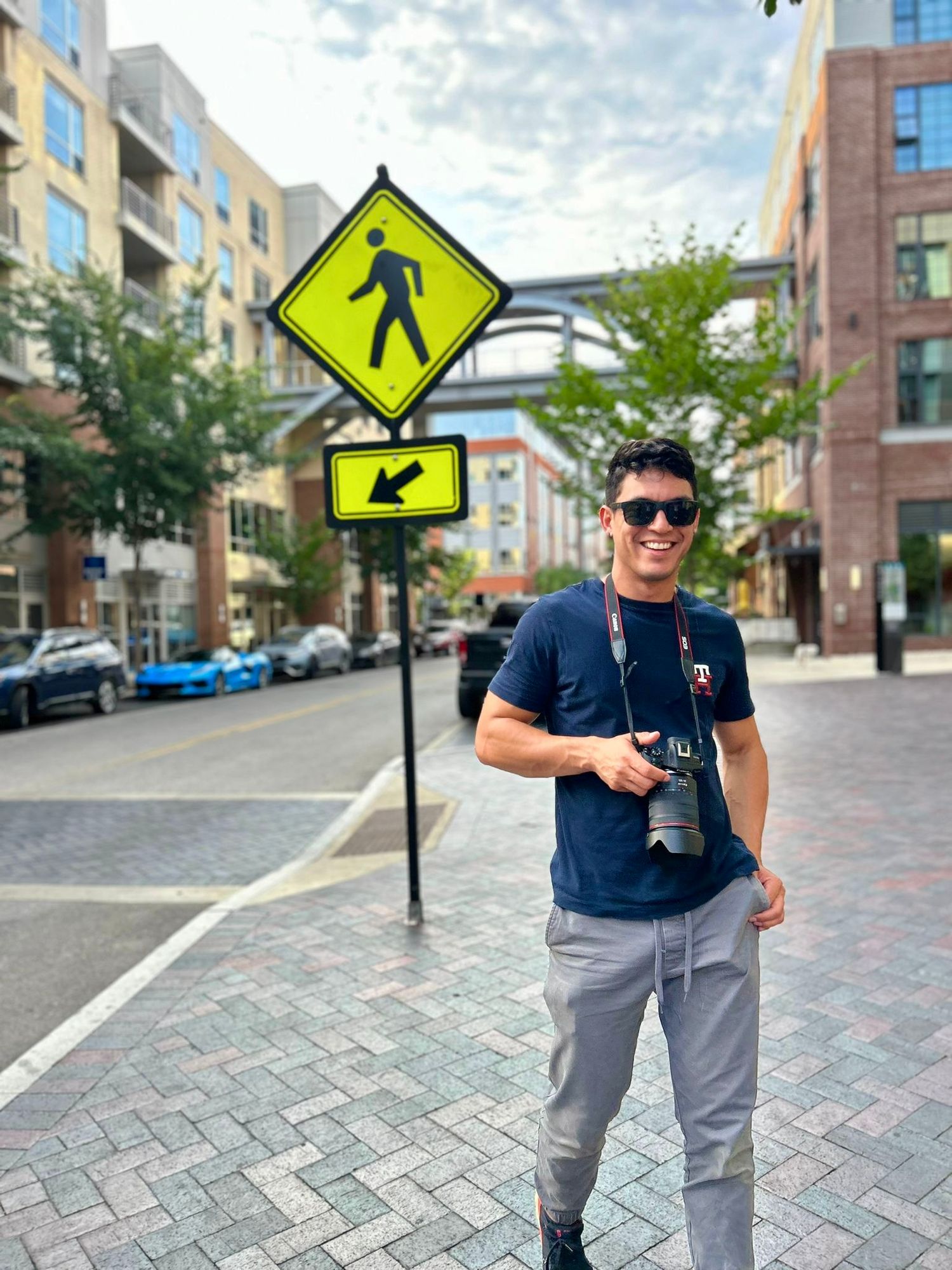 Photographer standing next to pedestrian crossing sign on urban street with apartment buildings.