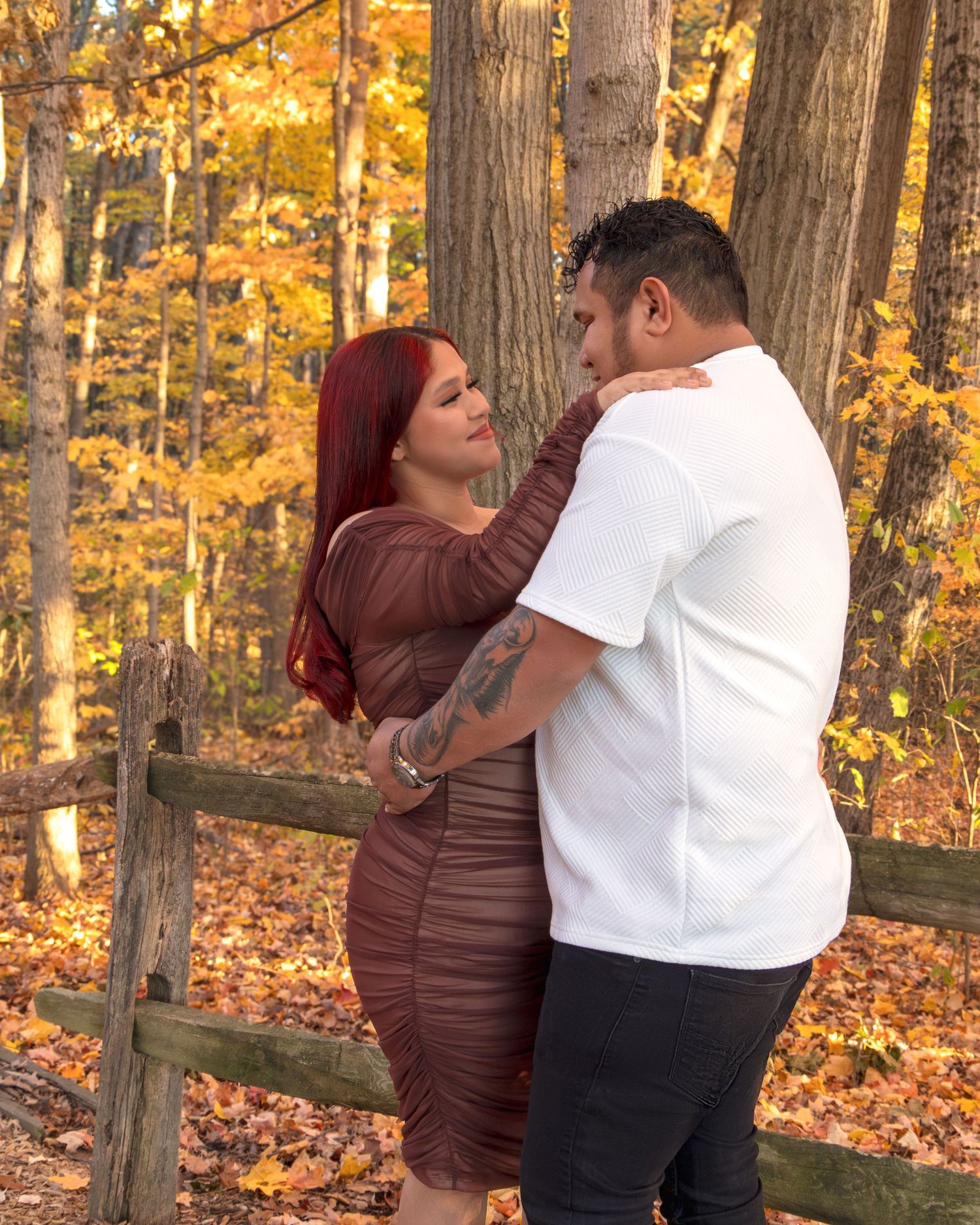 Couple embracing in autumn forest setting with golden foliage, woman in brown dress with red hair, man in white shirt.