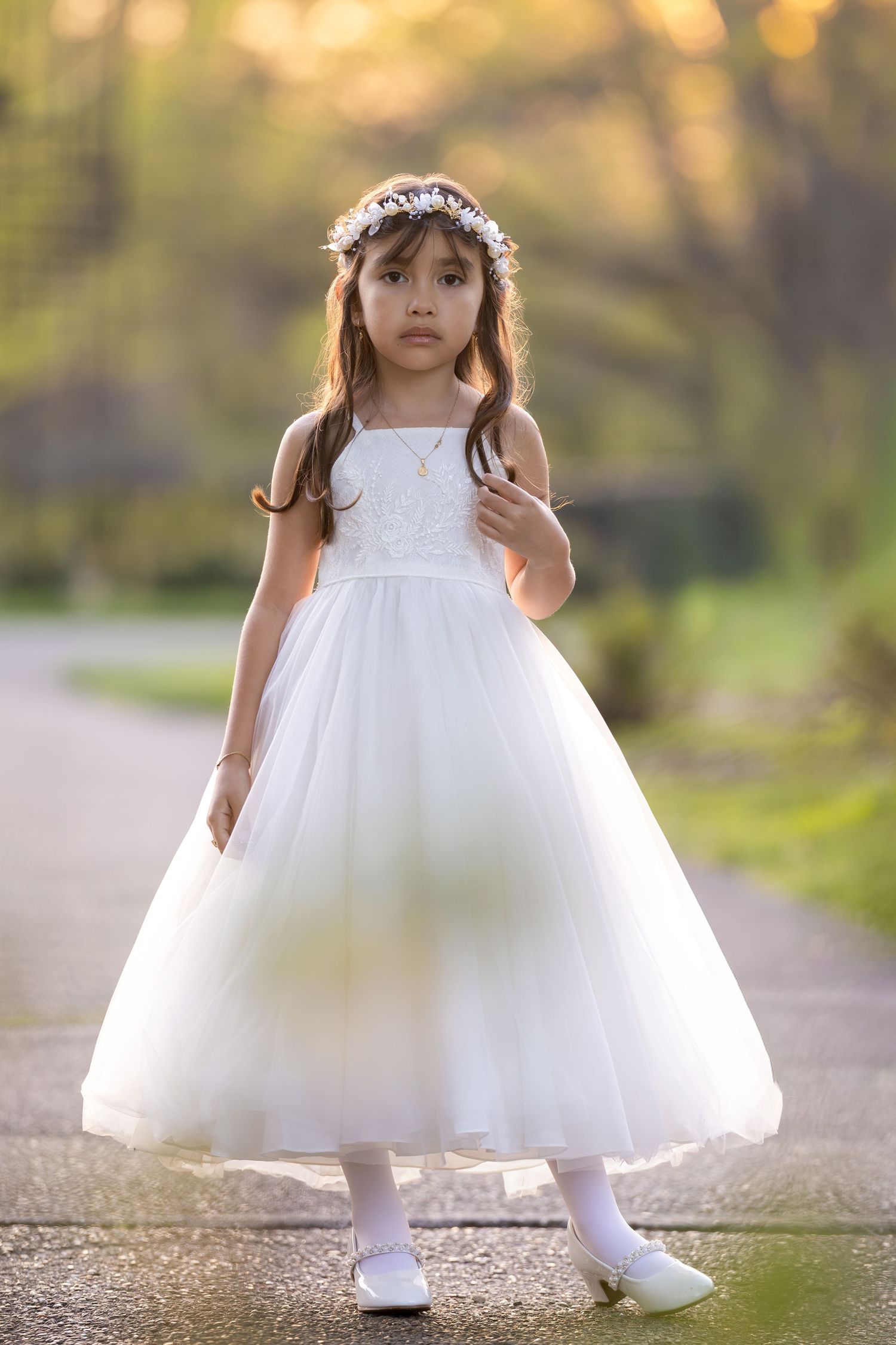 Young girl in white tulle dress and floral crown poses outdoors for First Communion portrait.