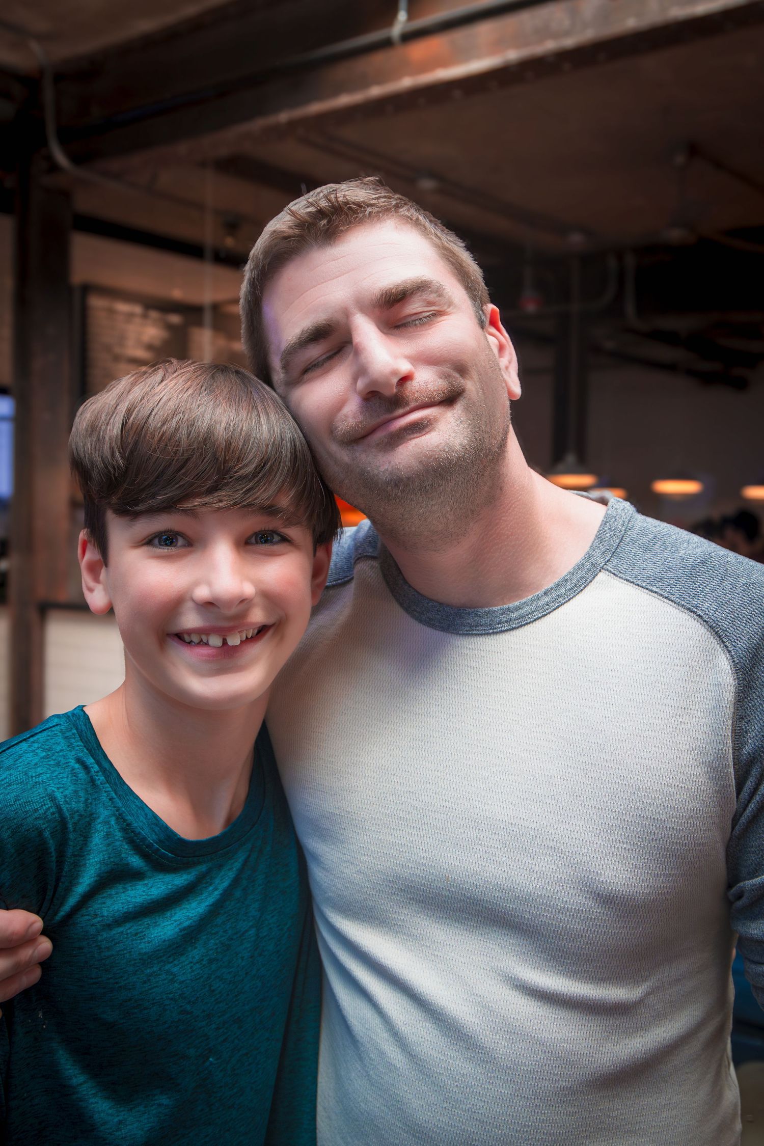 Two people share a close embrace and bright smiles in a dimly lit indoor space.