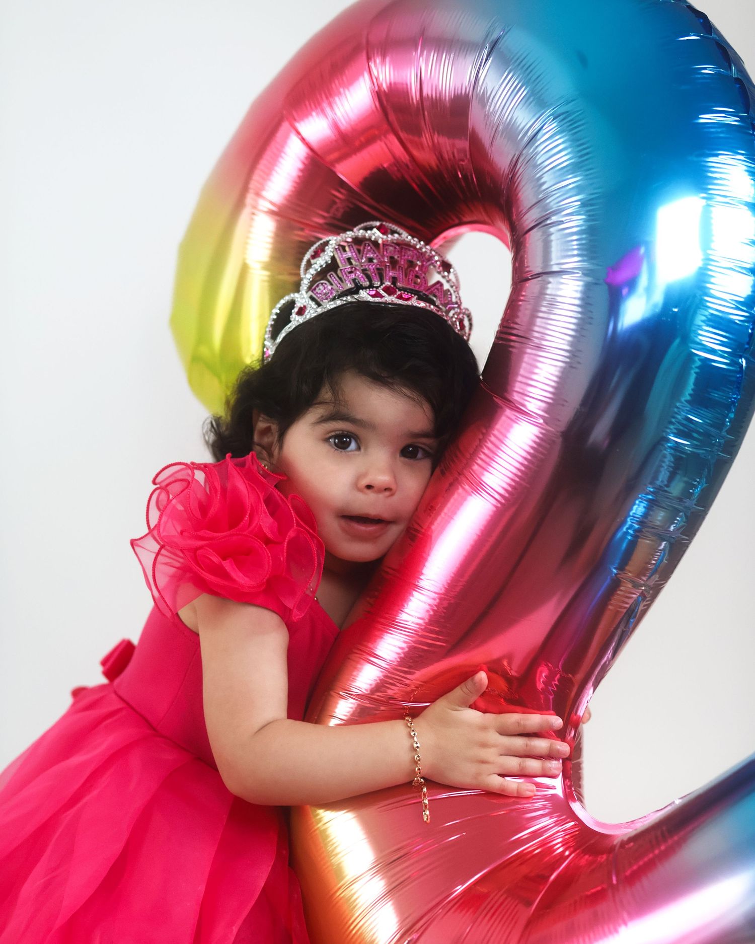 Pink dress and tiara against colorful metallic number balloon backdrop.