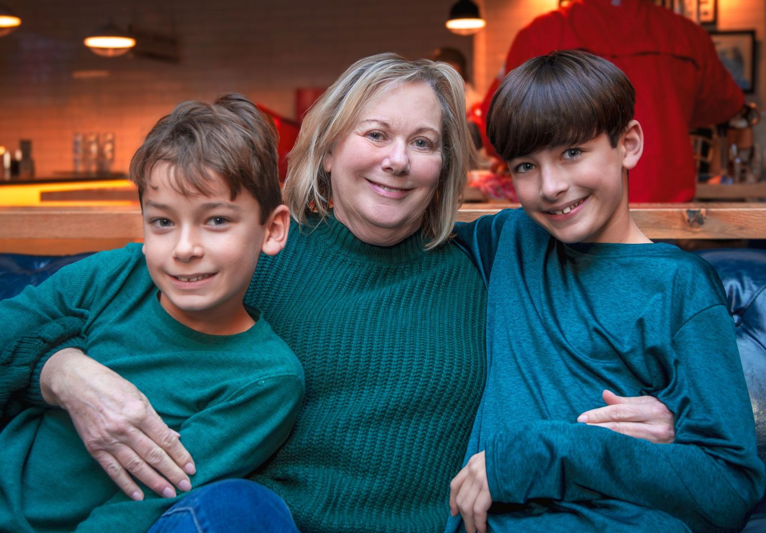 Family portrait of three people wearing matching green sweaters sitting together indoors.