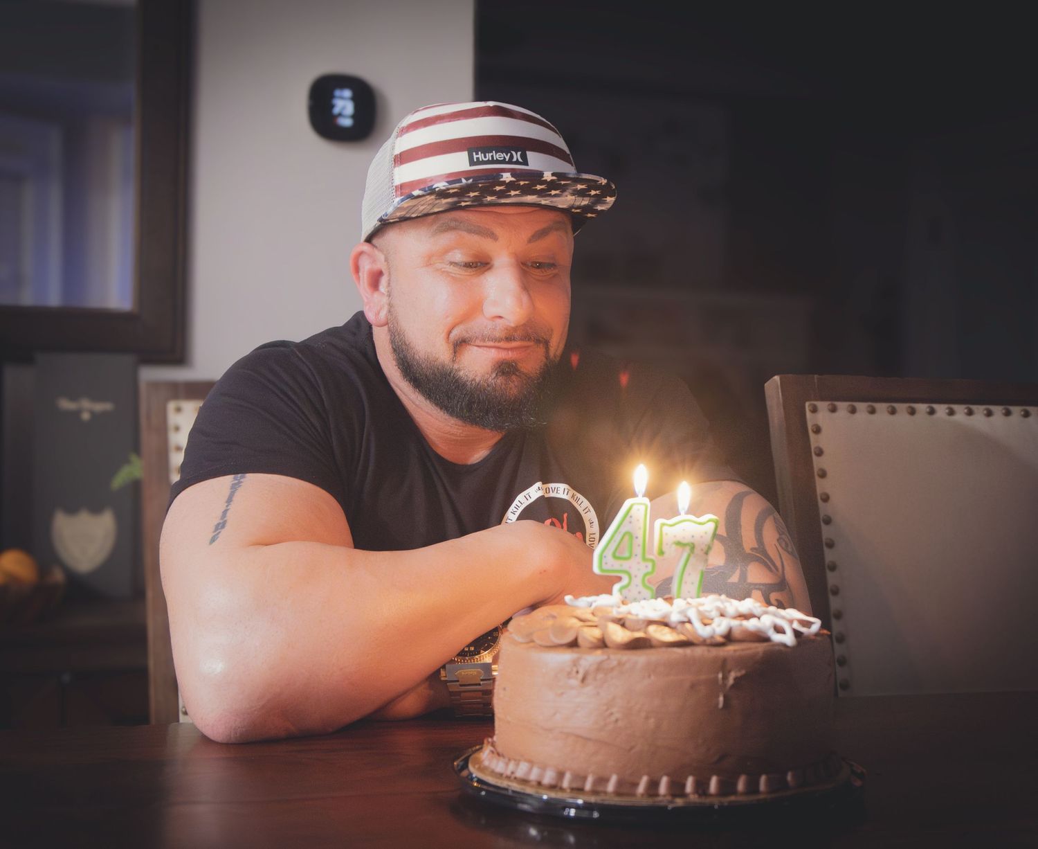 Person making wish over chocolate birthday cake with lit candles in dark room.