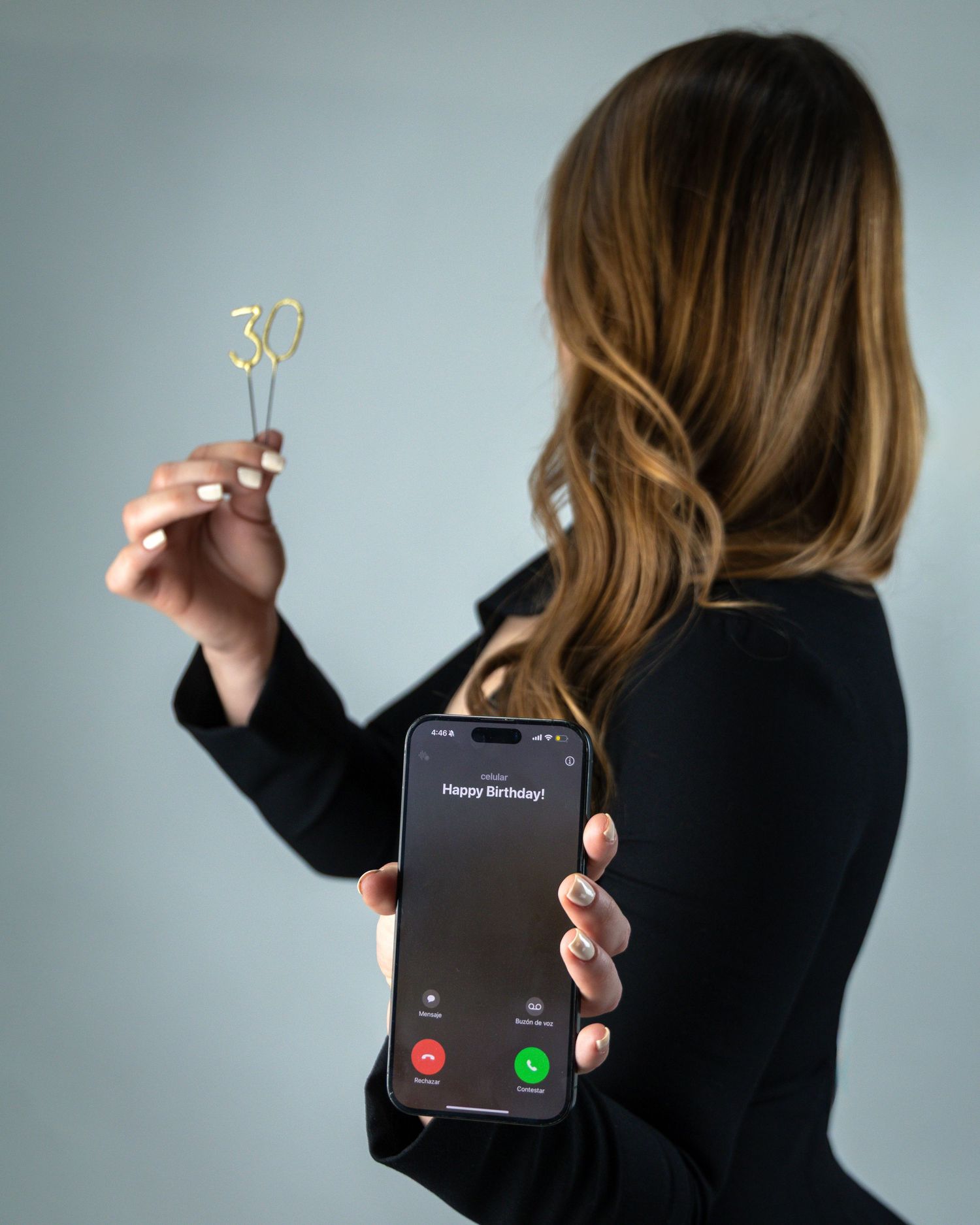 Woman holding a phone with Happy Birthday incoming call and a gold number 30 candle, celebrating her 30th birthday.