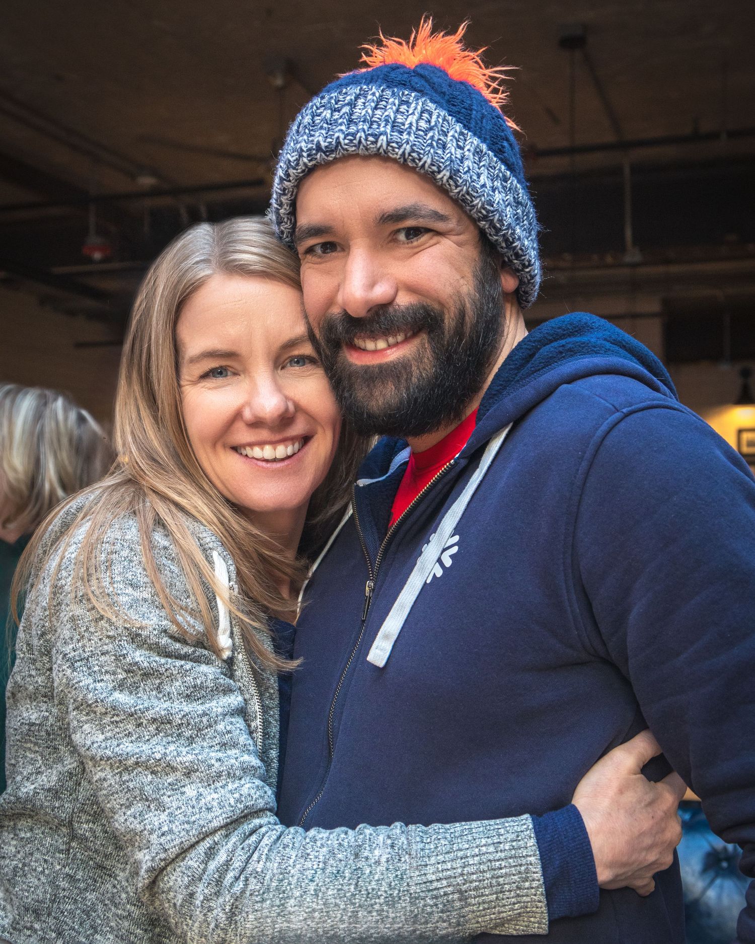 Couple embracing and smiling, with one wearing a blue knit winter hat with orange pom-pom.
