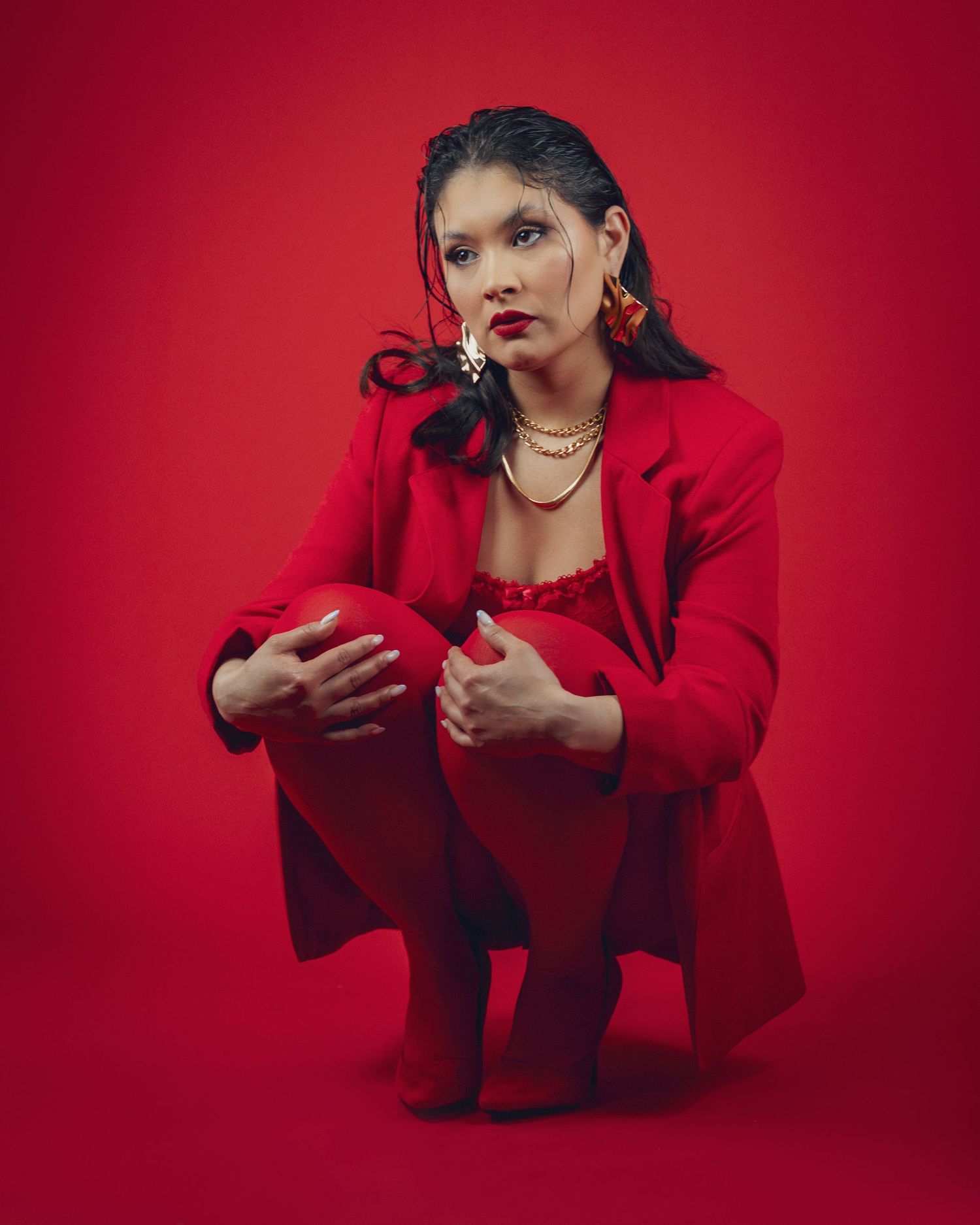 Woman in red blazer and matching outfit poses confidently against a red background with gold jewelry.