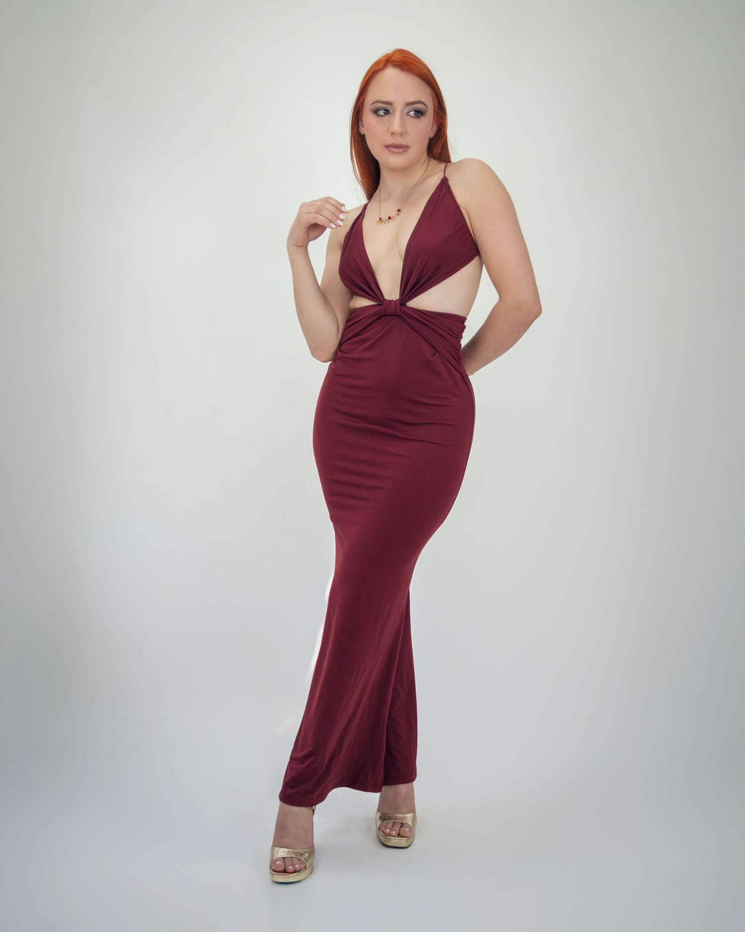 Woman in burgundy halter maxi dress with cutout detail and side slit, paired with nude heels.