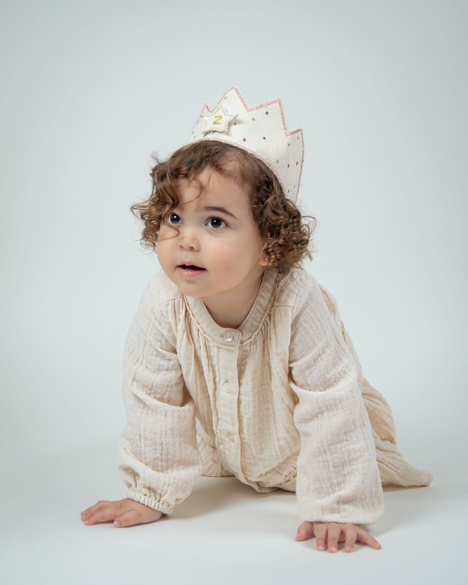 A baby in a cozy cream sweater crawls and explores on a light gray background in a photo series.