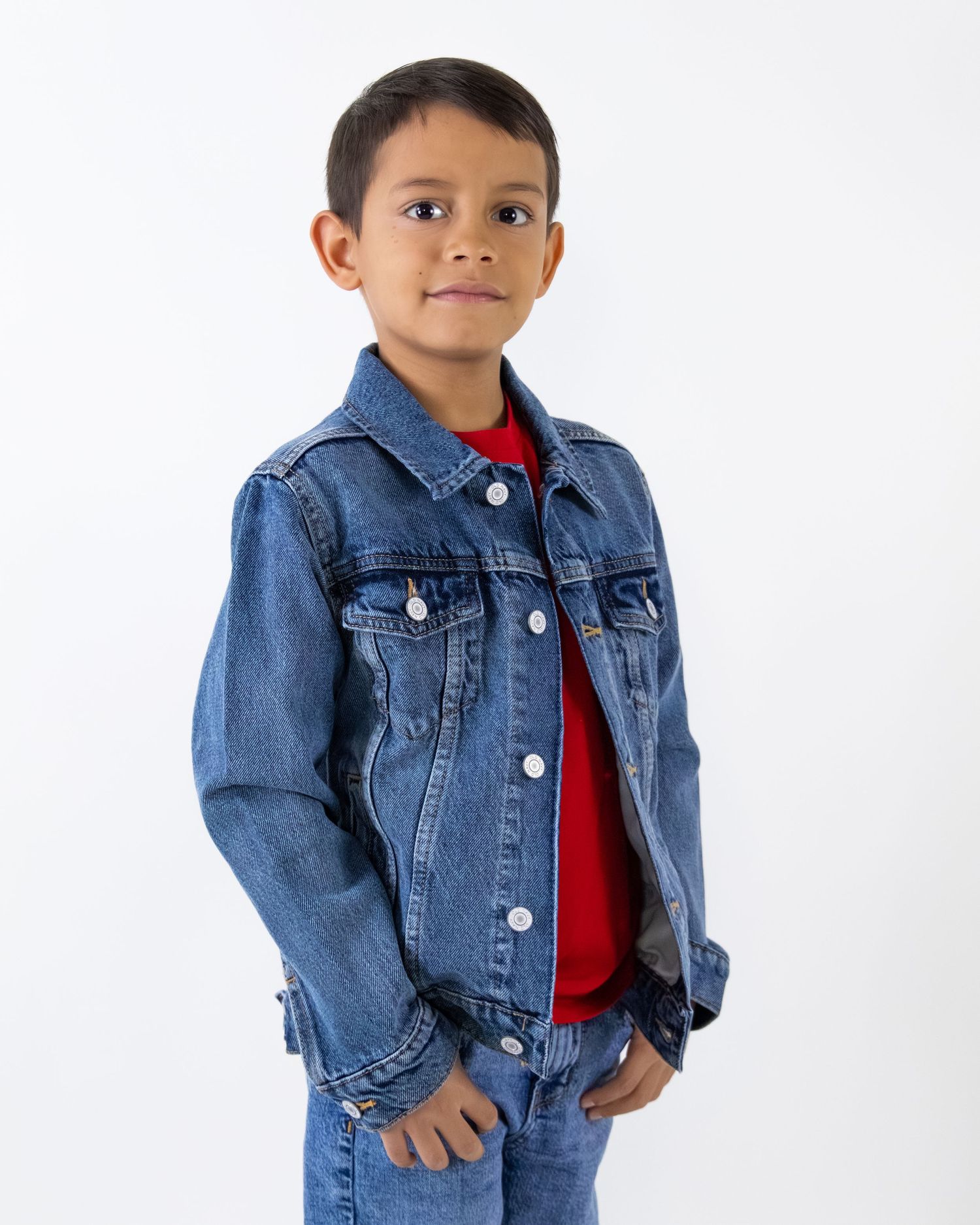 Young boy wearing a blue denim jacket over a red shirt with matching jeans, posing confidently.