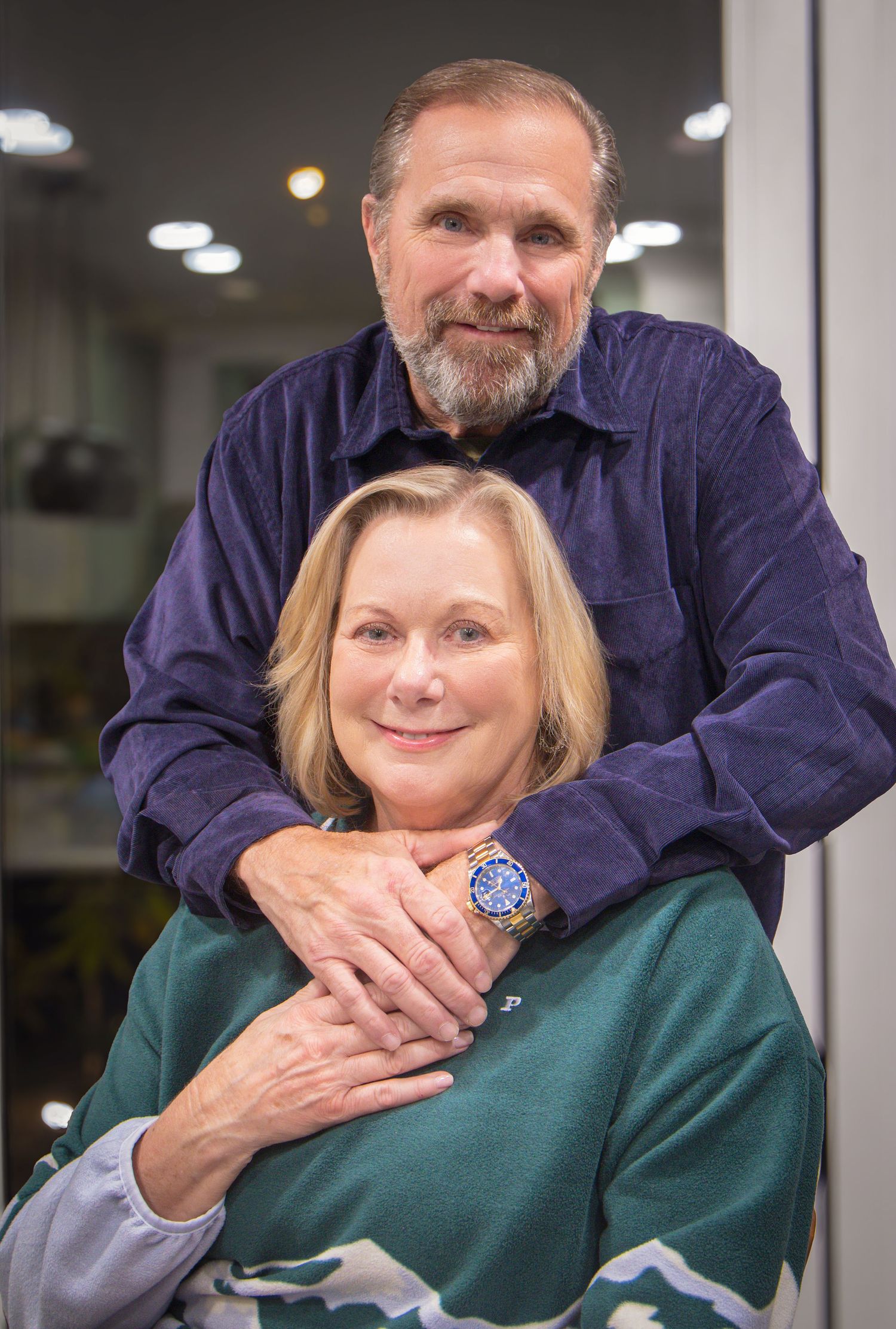 Two people posing together in an indoor setting with ceiling lights visible in the background.