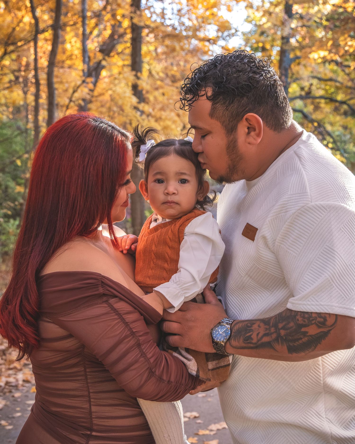 A tender family moment captured in autumn with warm earth tones and fall foliage in the background.