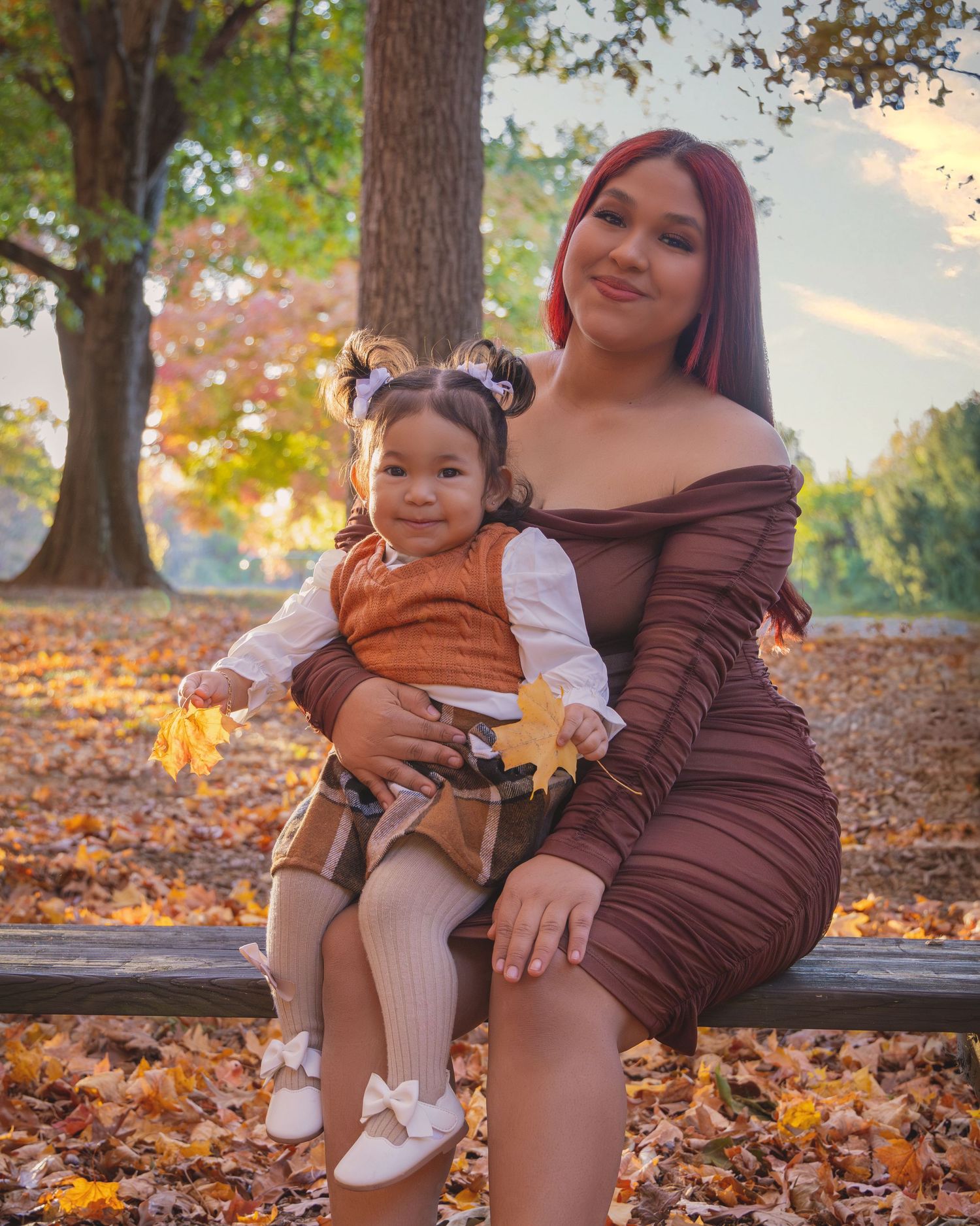 Mother and child sitting on bench surrounded by fall foliage.