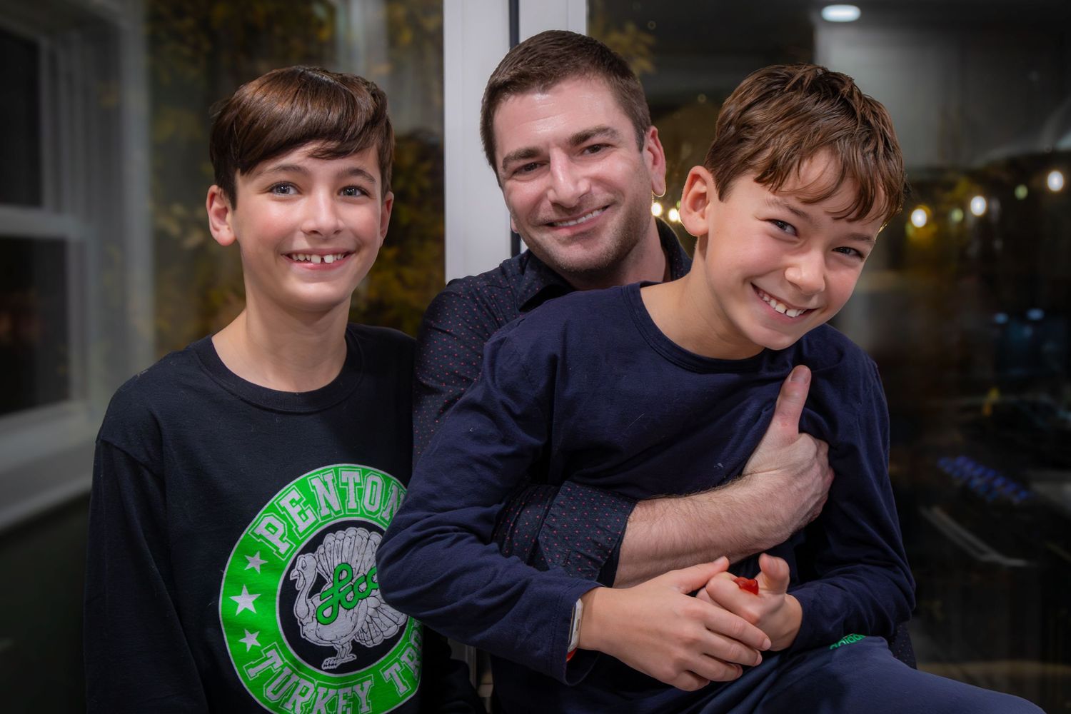 A man smiles with two young boys in a warmly lit room.